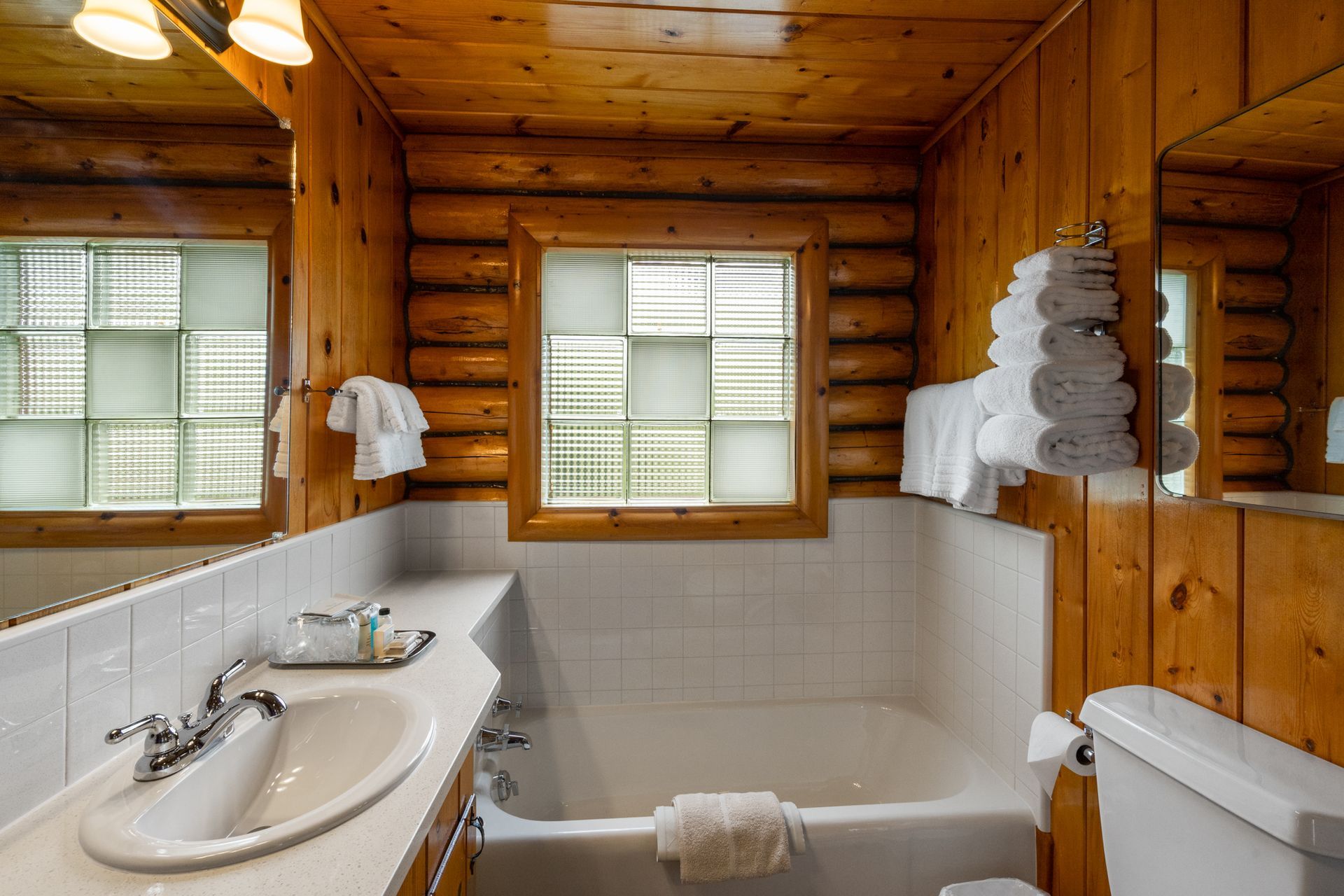 A bathroom in a log cabin with a tub , sink , toilet and mirror.