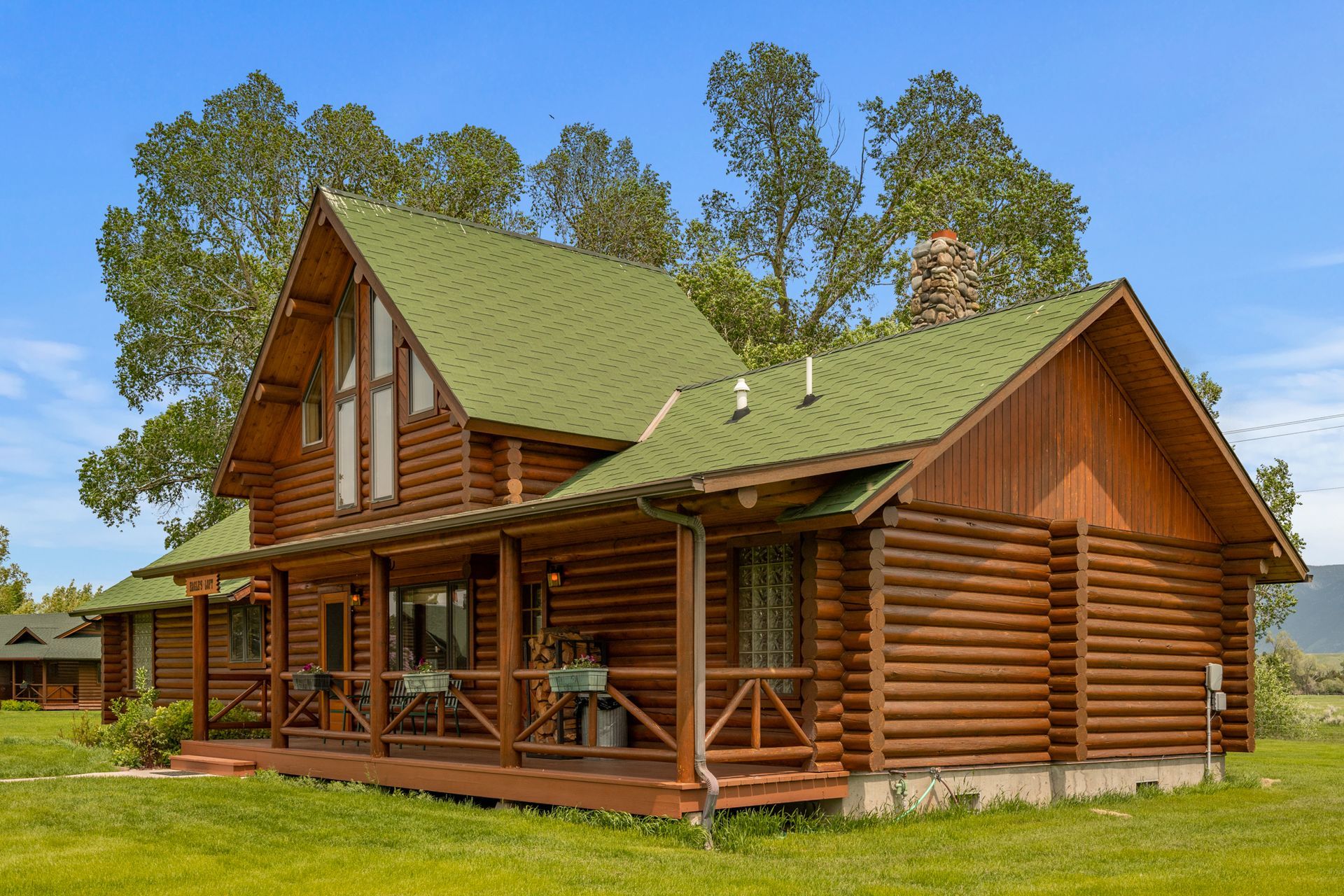 A large log cabin with a green roof is sitting on top of a lush green field.