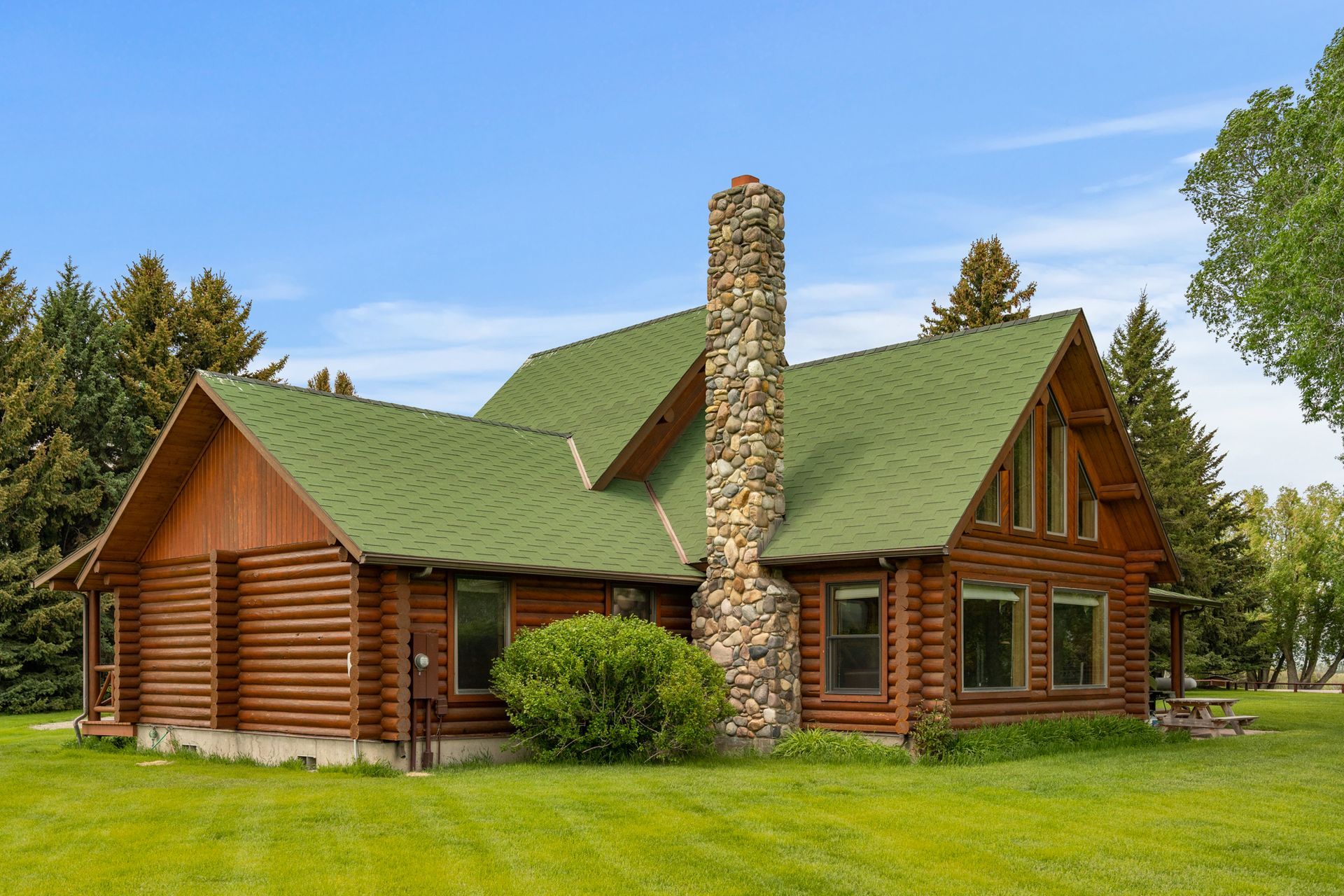 A log cabin with a green roof and a stone chimney