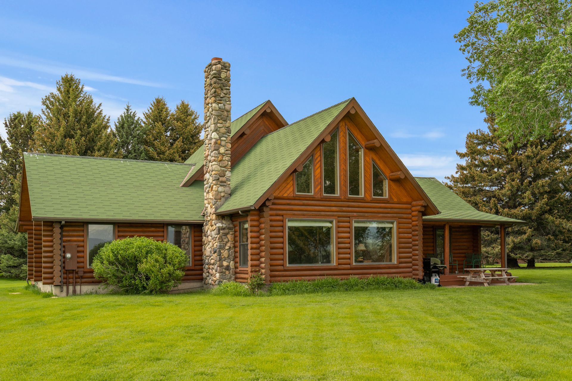 A large log cabin with a green roof is sitting in the middle of a lush green field.