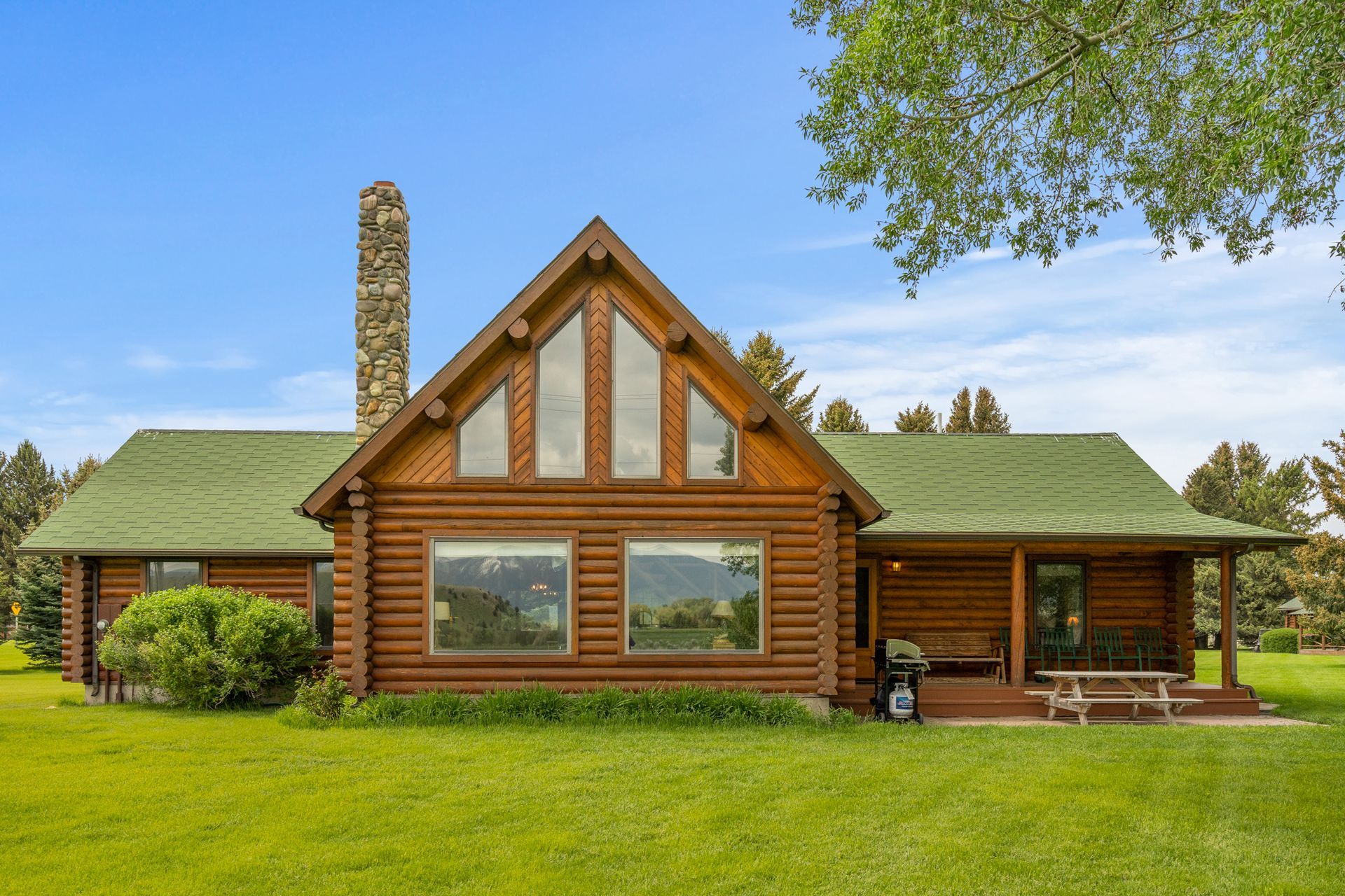 A large log cabin with a green roof and a chimney
