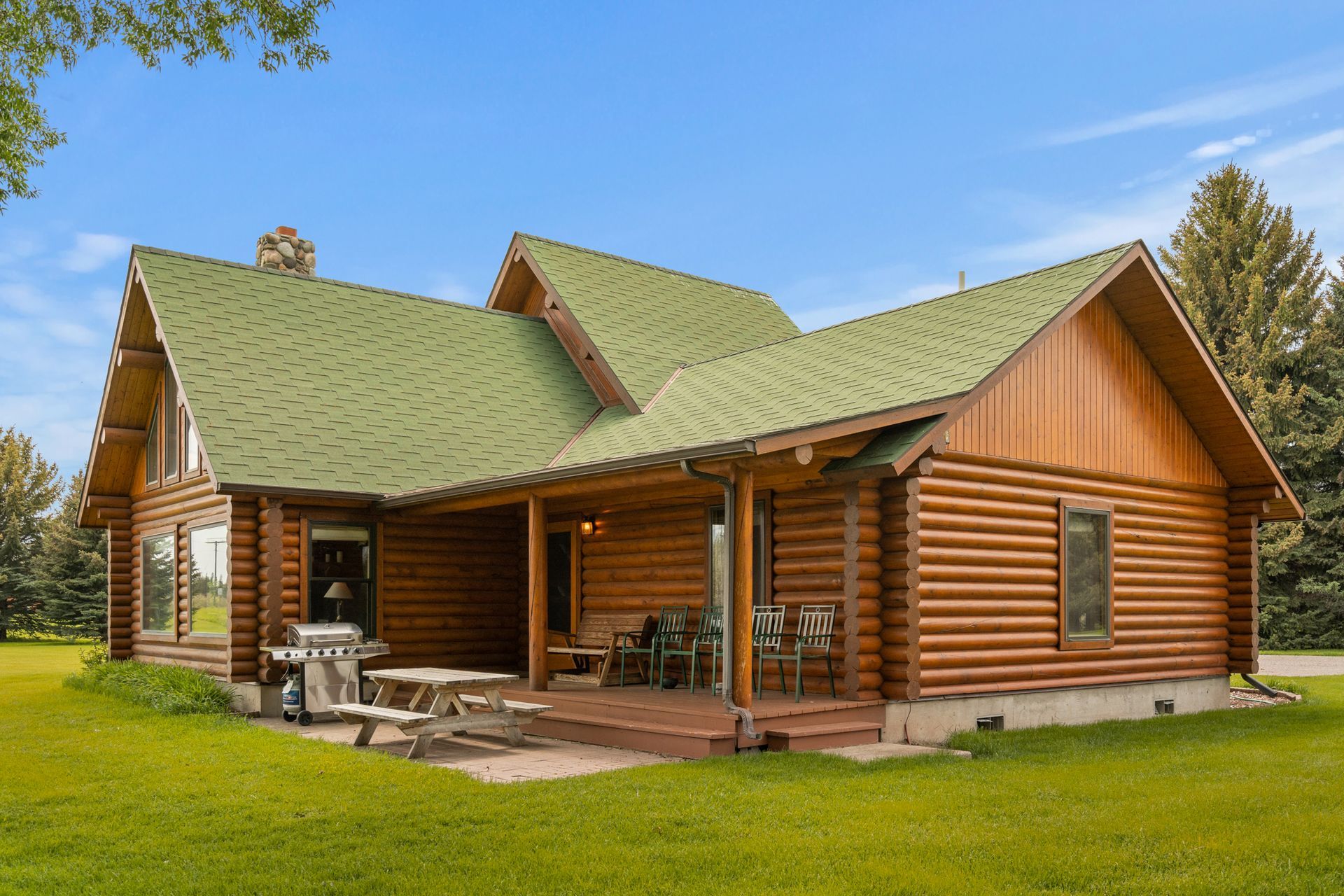 A log cabin with a green roof and a picnic table