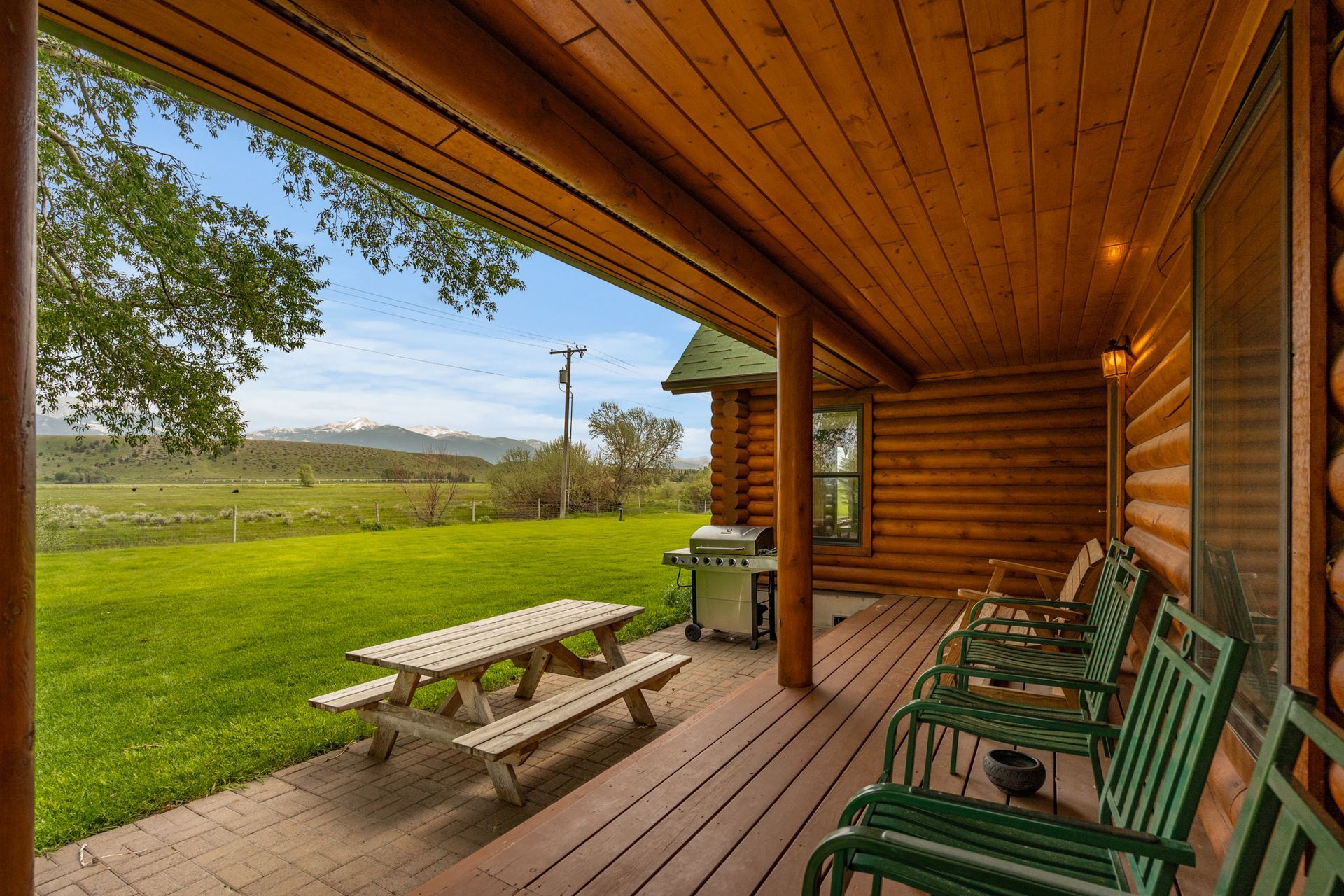 There is a picnic table and chairs on the porch of a log cabin.