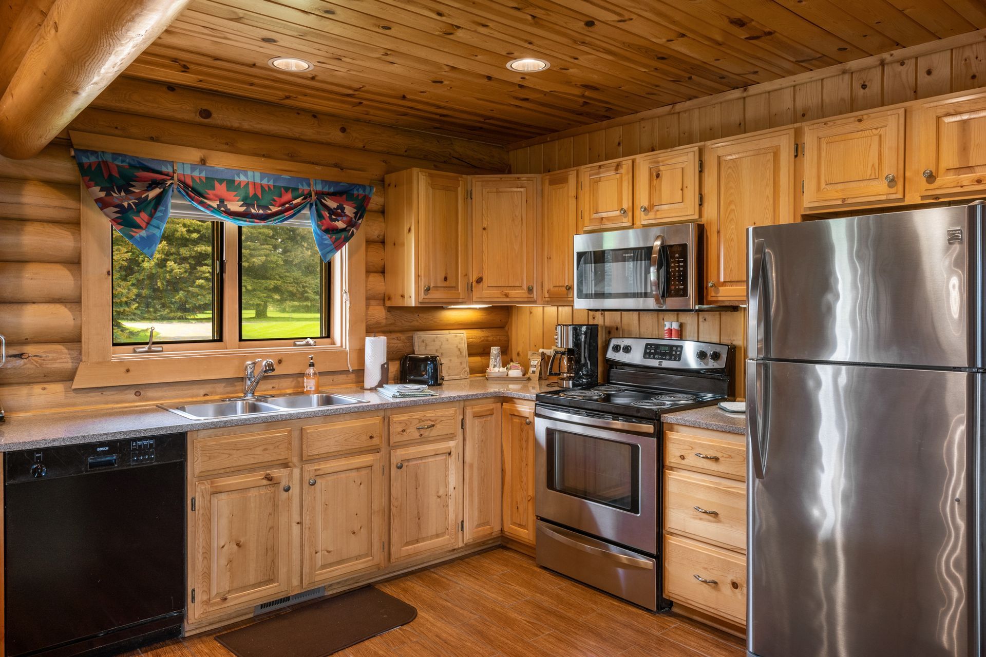 A kitchen in a log cabin with stainless steel appliances and wooden cabinets.