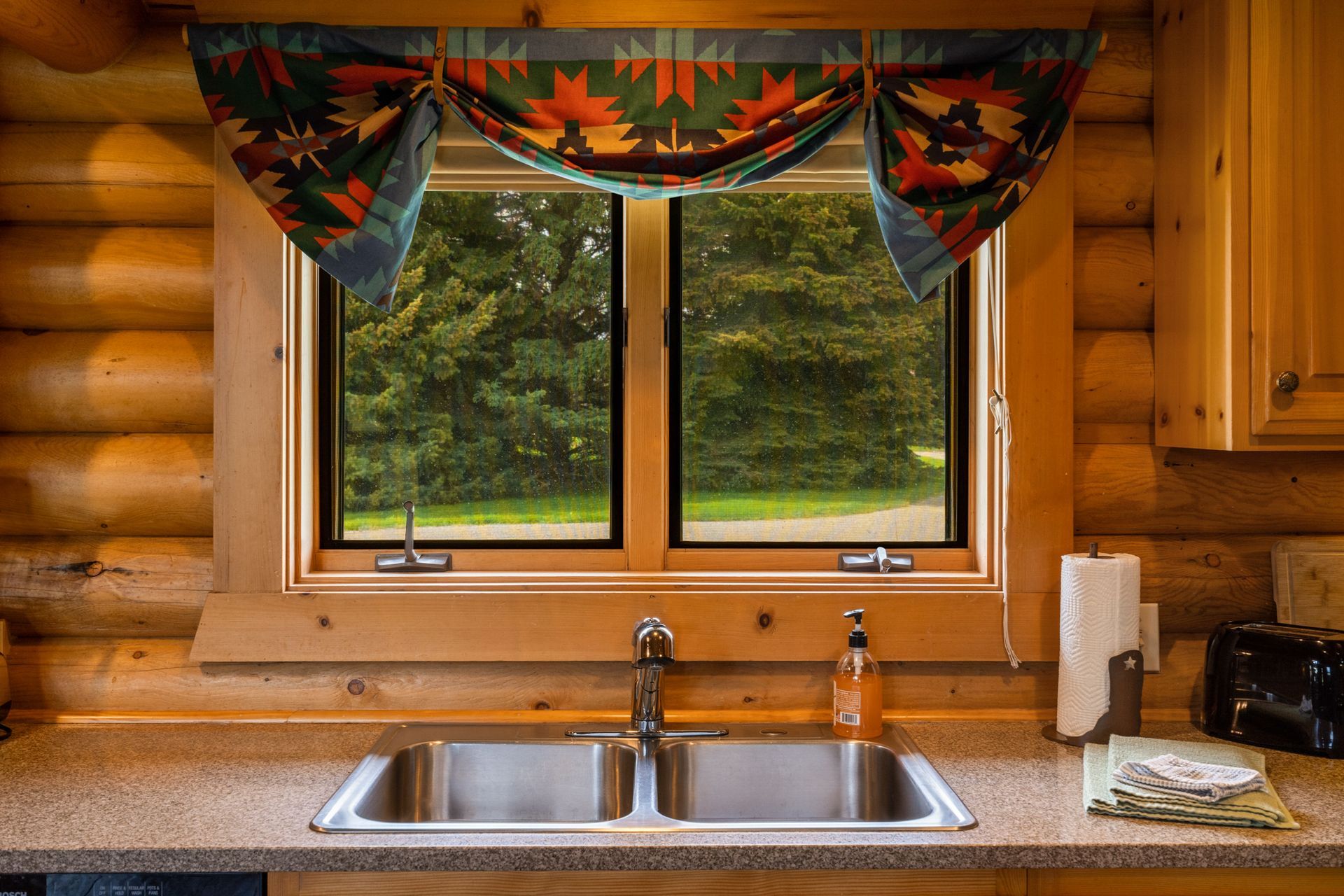 A kitchen sink in a log cabin with a large window.