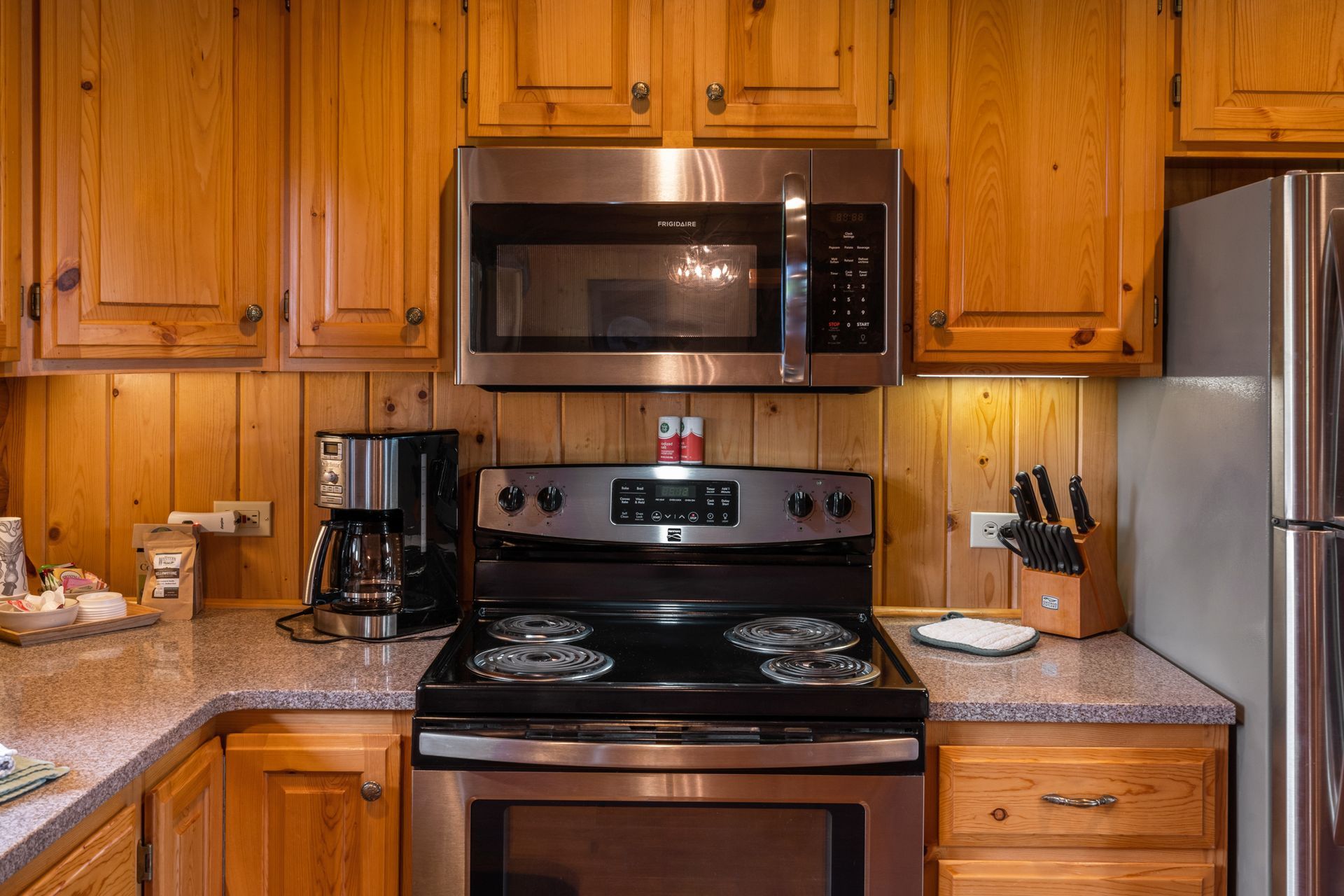 A kitchen with a stove , microwave , refrigerator and wooden cabinets.