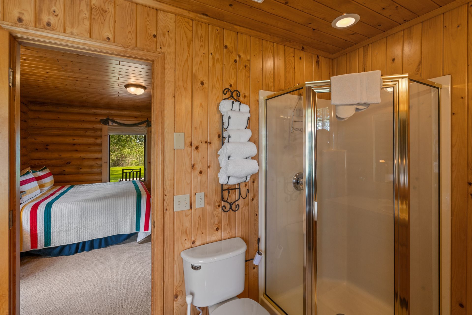 A bathroom in a log cabin with a toilet , shower and bed.