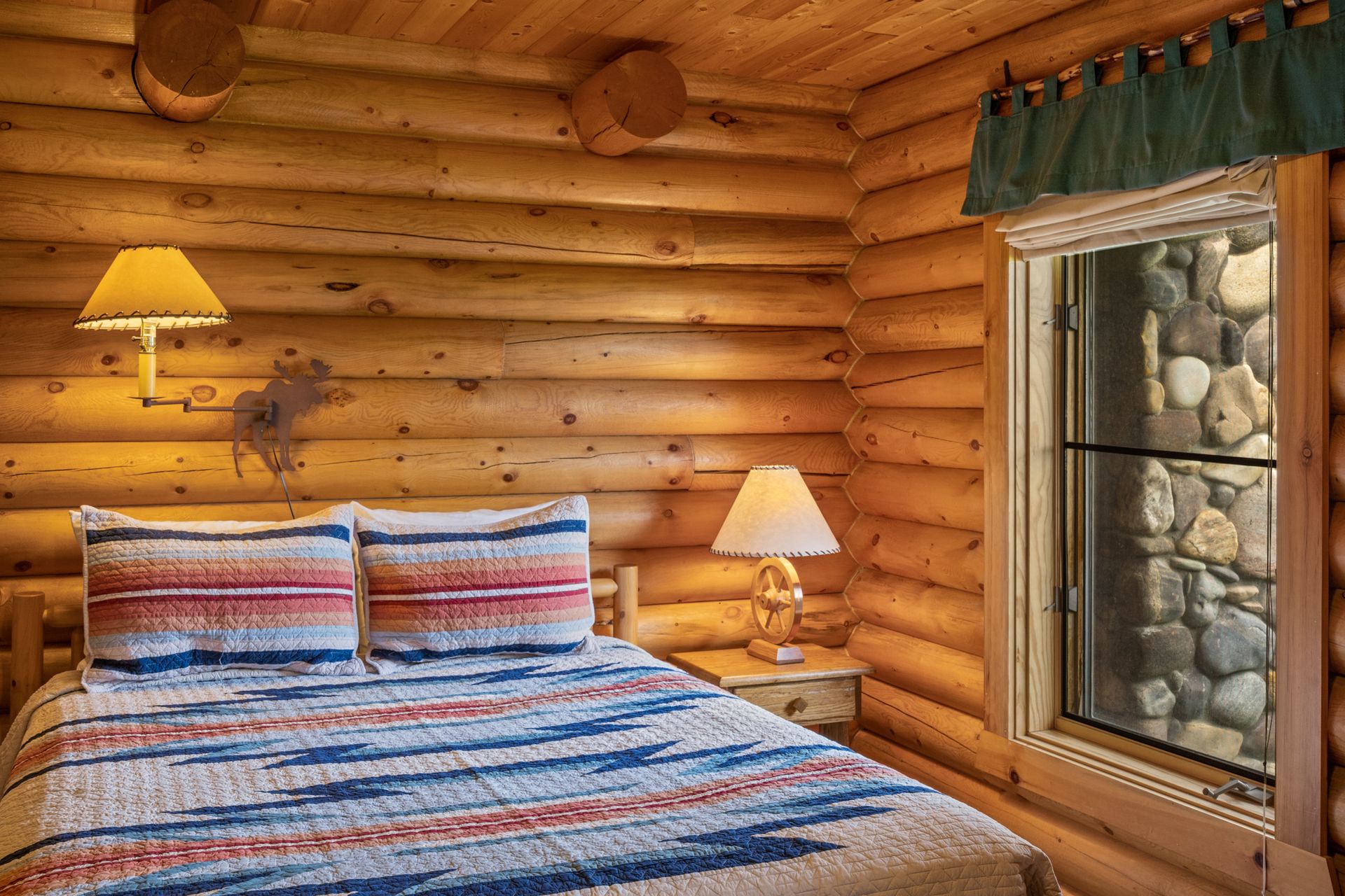 A bedroom in a log cabin with a bed , lamps , and a window.