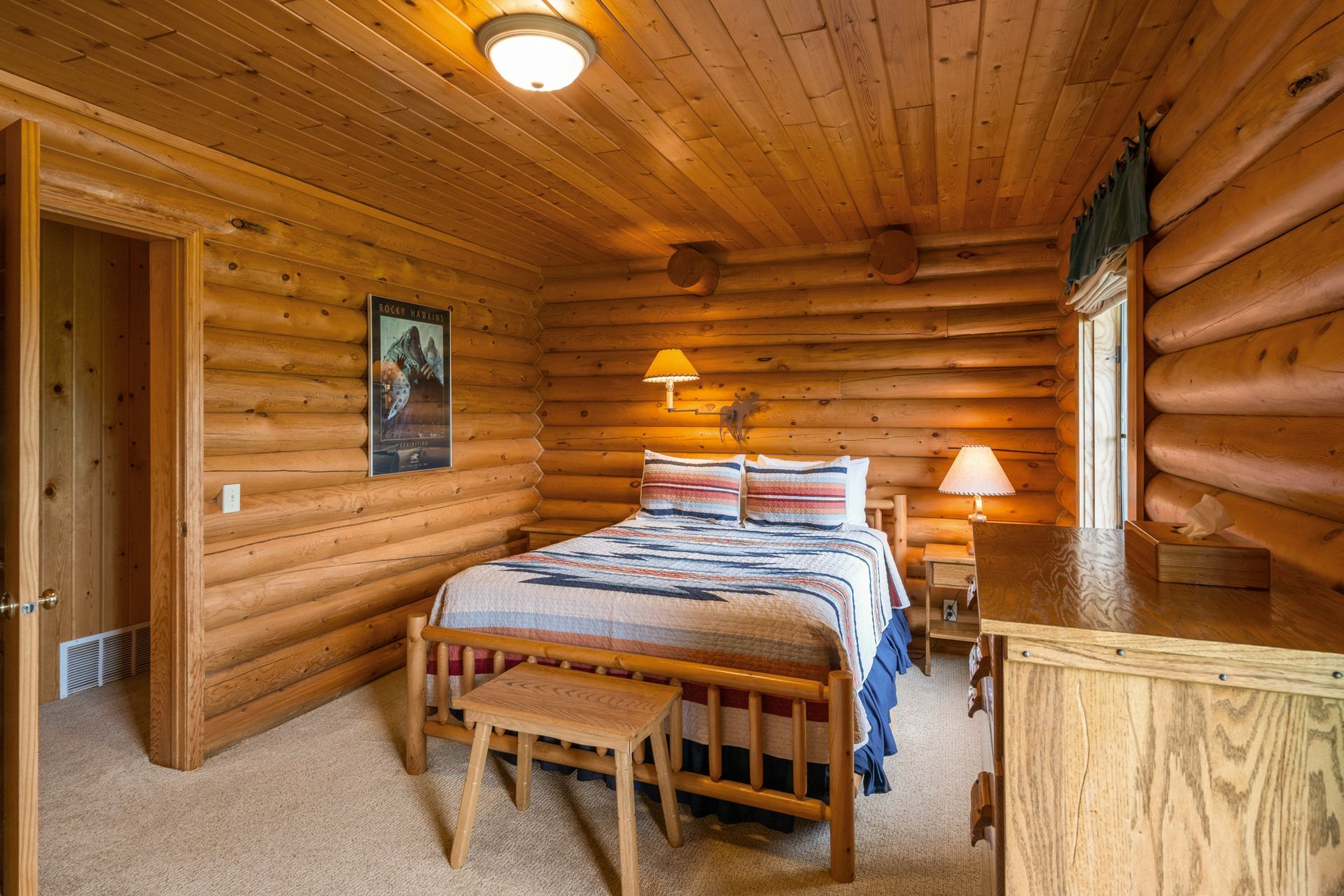 A bedroom in a log cabin with a bed and dresser.