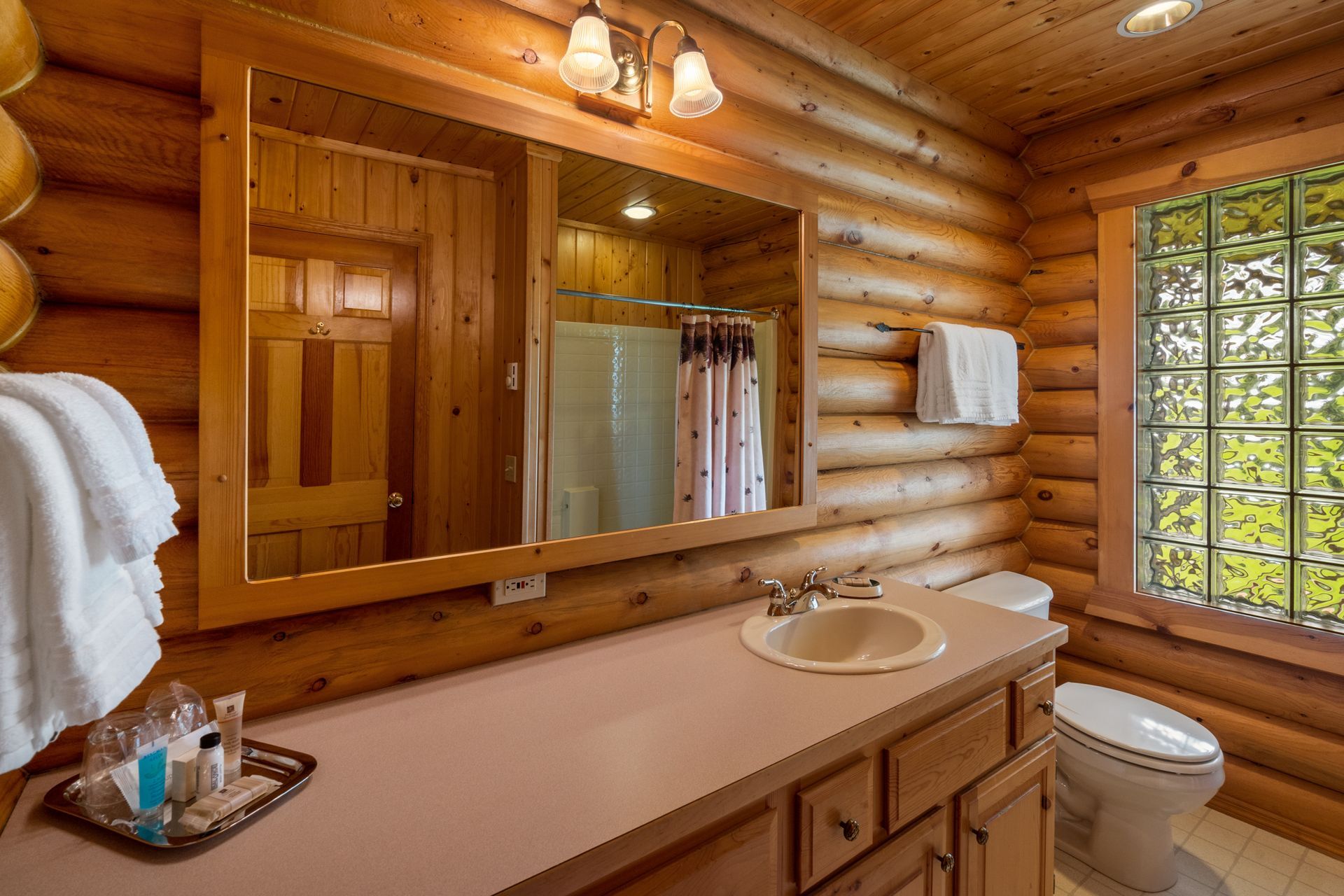 A bathroom in a log cabin with a sink , toilet and mirror.