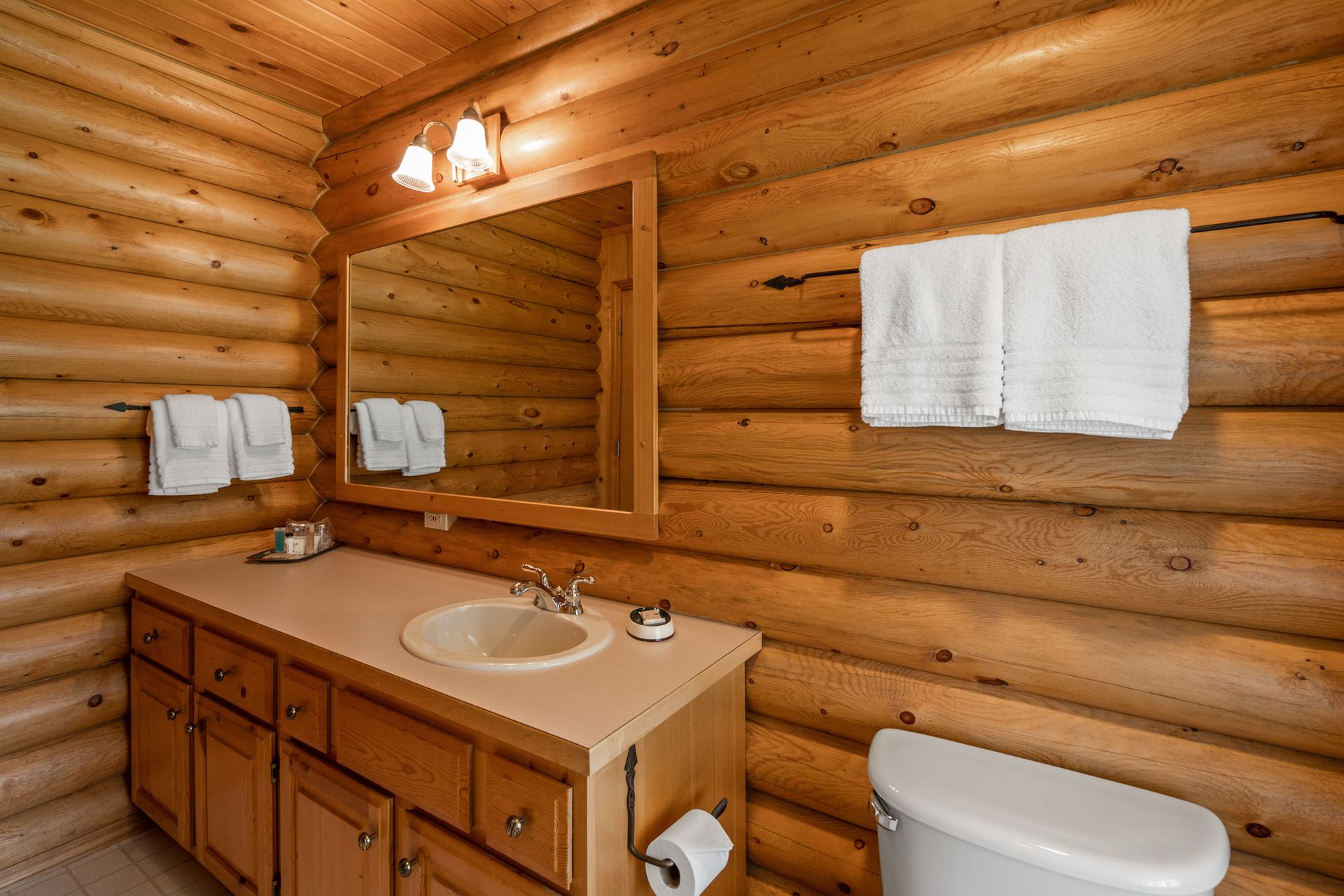 A bathroom in a log cabin with a sink , toilet and mirror.