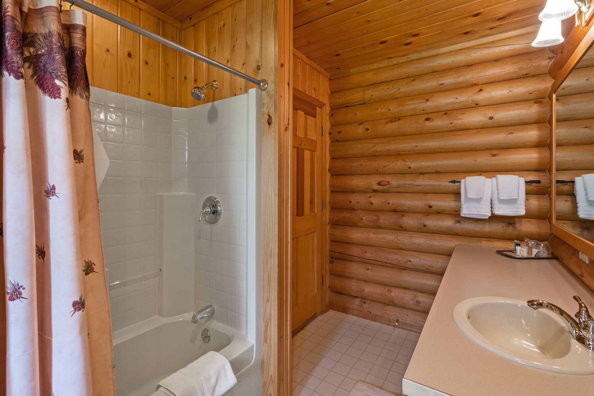 A bathroom in a log cabin with a tub , sink and shower.