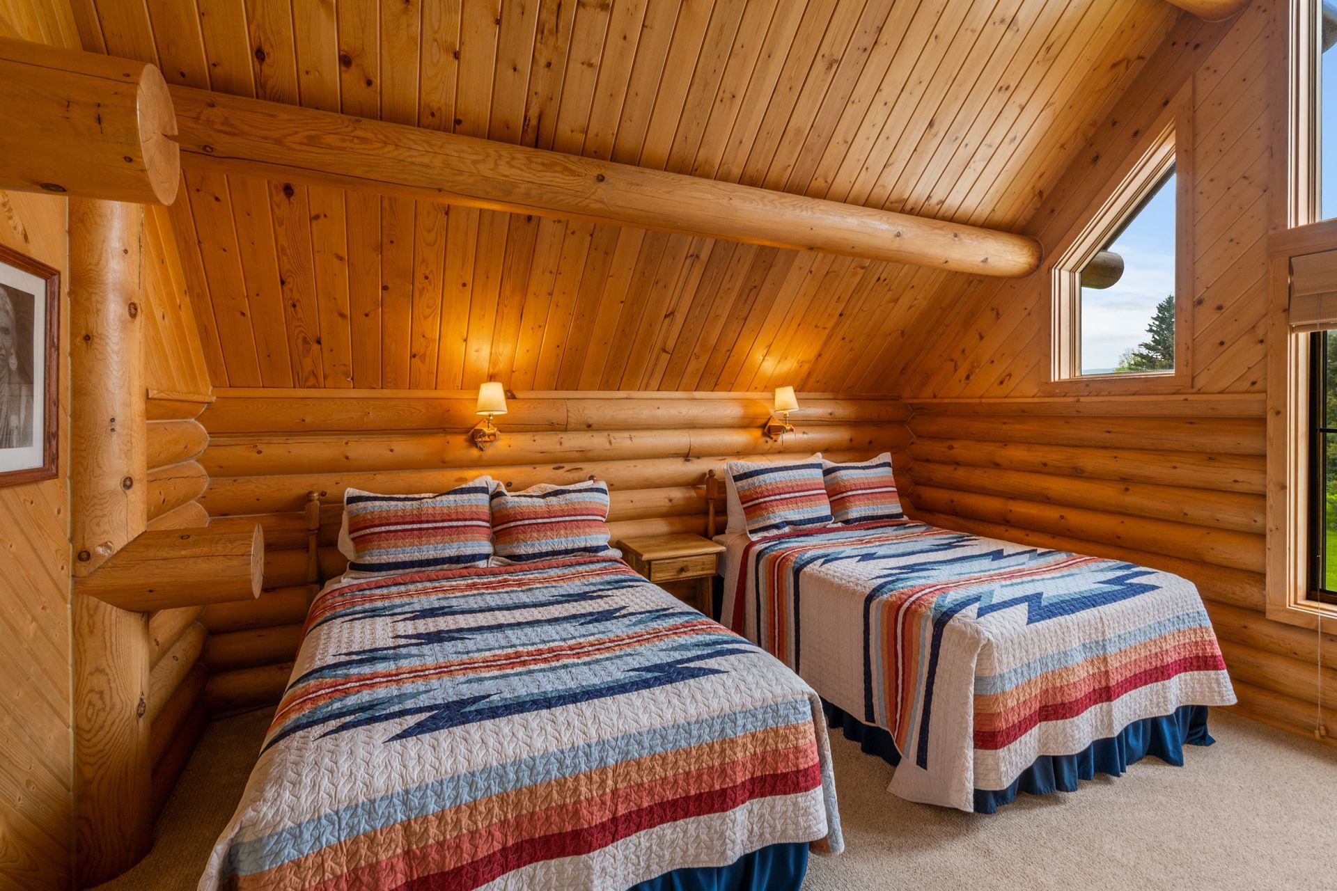 A bedroom in a log cabin with two beds and a window.