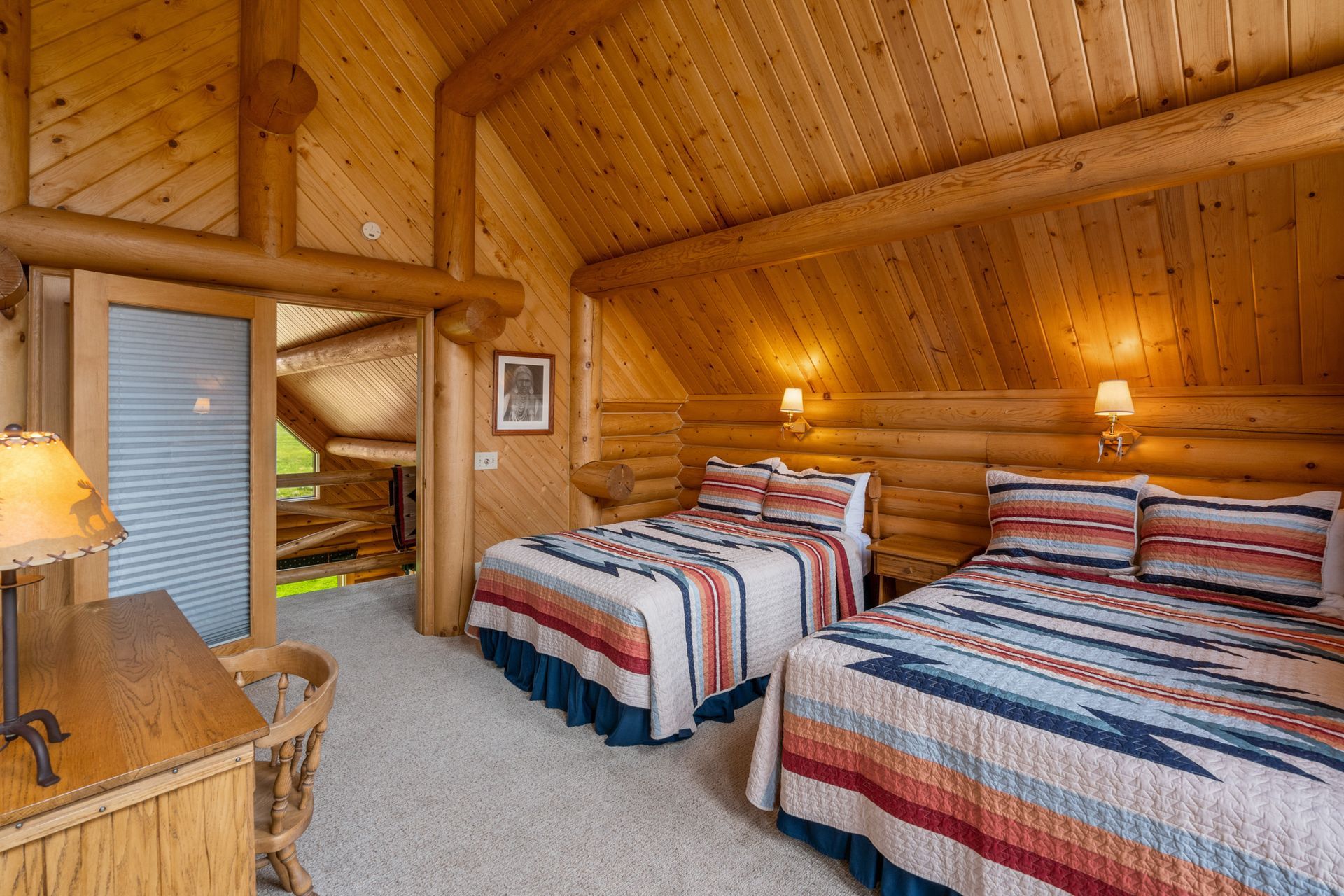 A bedroom in a log cabin with two beds and a desk.