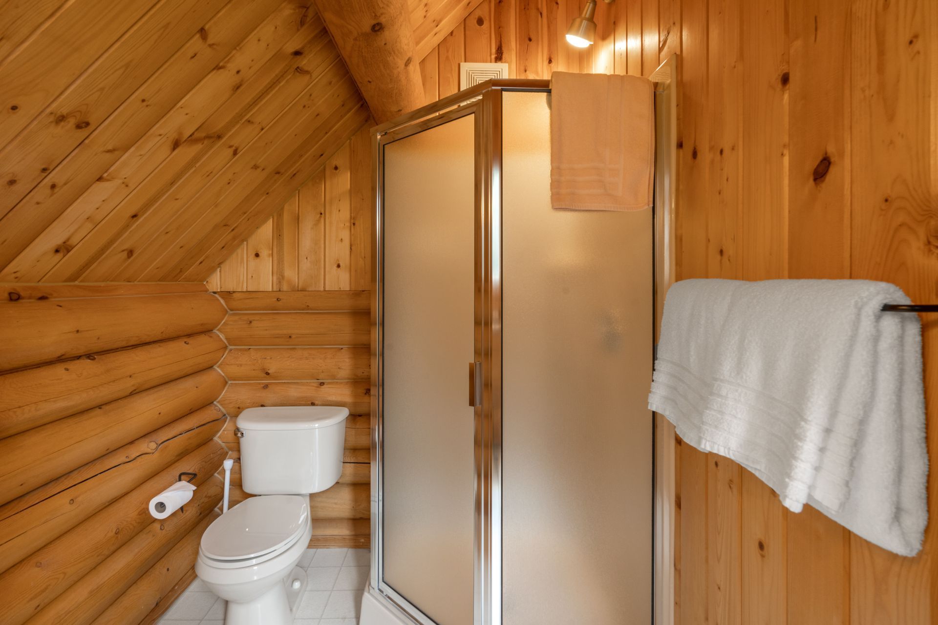 A bathroom in a log cabin with a toilet , shower and towels.