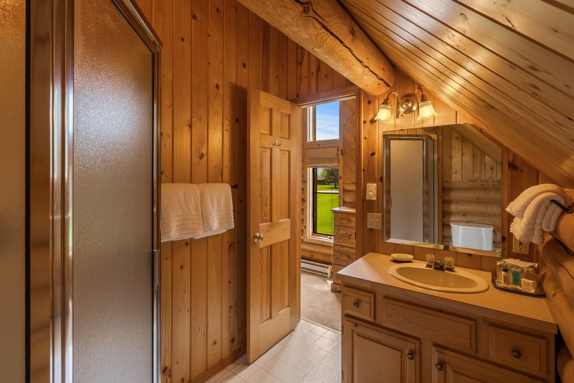 A bathroom in a log cabin with a sink , mirror and shower.