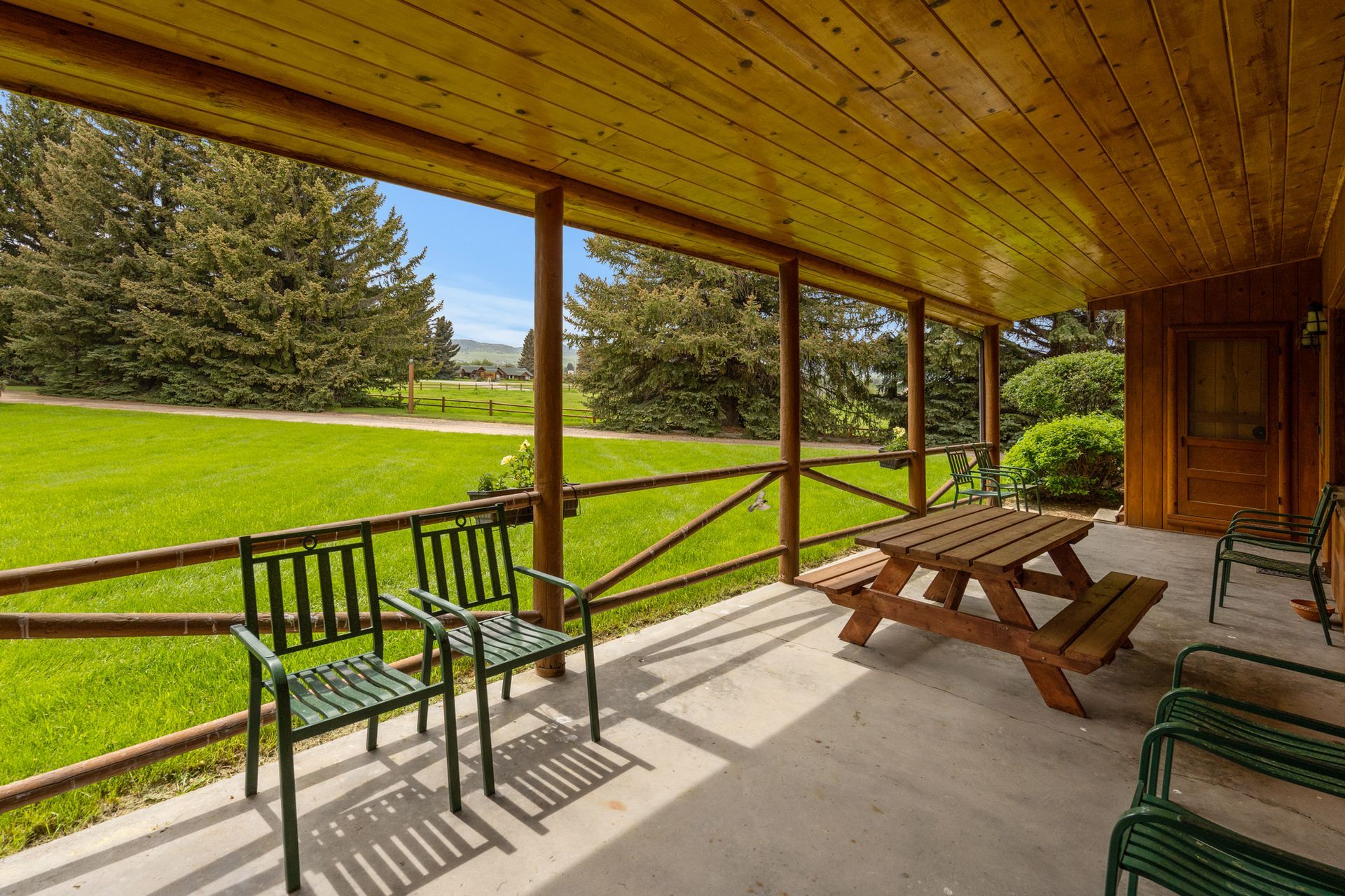 A porch with a picnic table and chairs overlooking a grassy field.