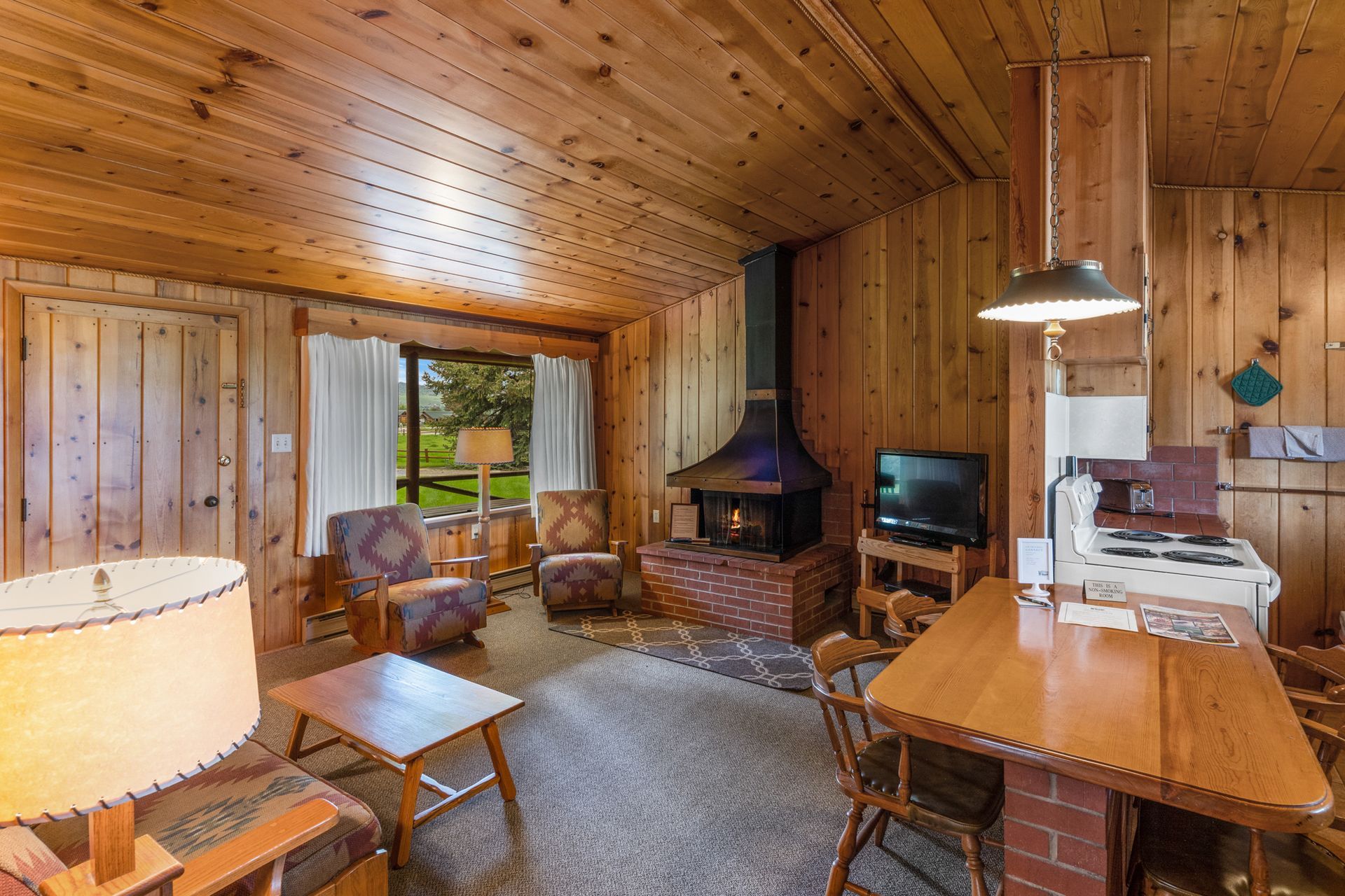 A living room in a cabin with wood paneling and a fireplace.