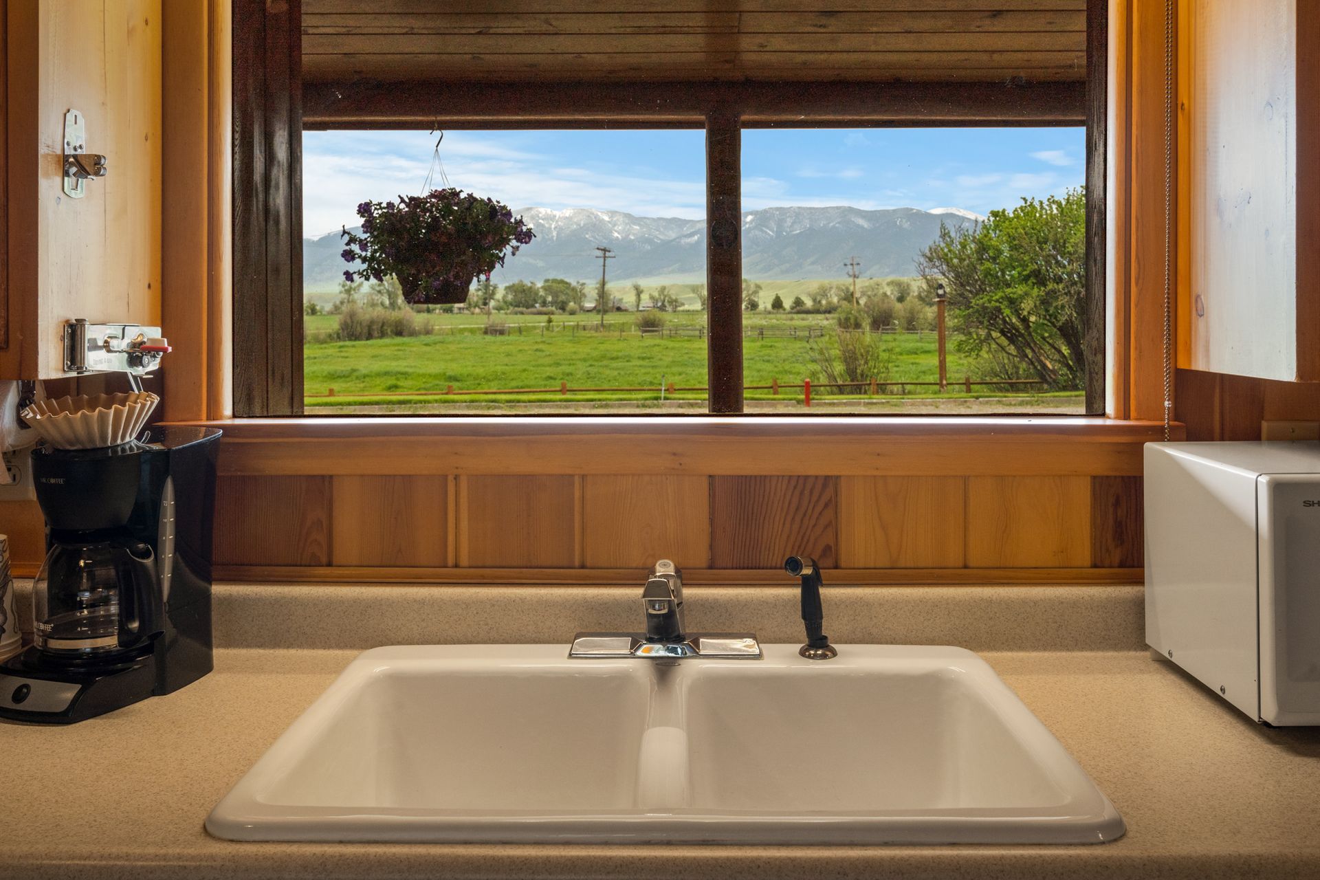 A kitchen sink with a view of a field through a window.