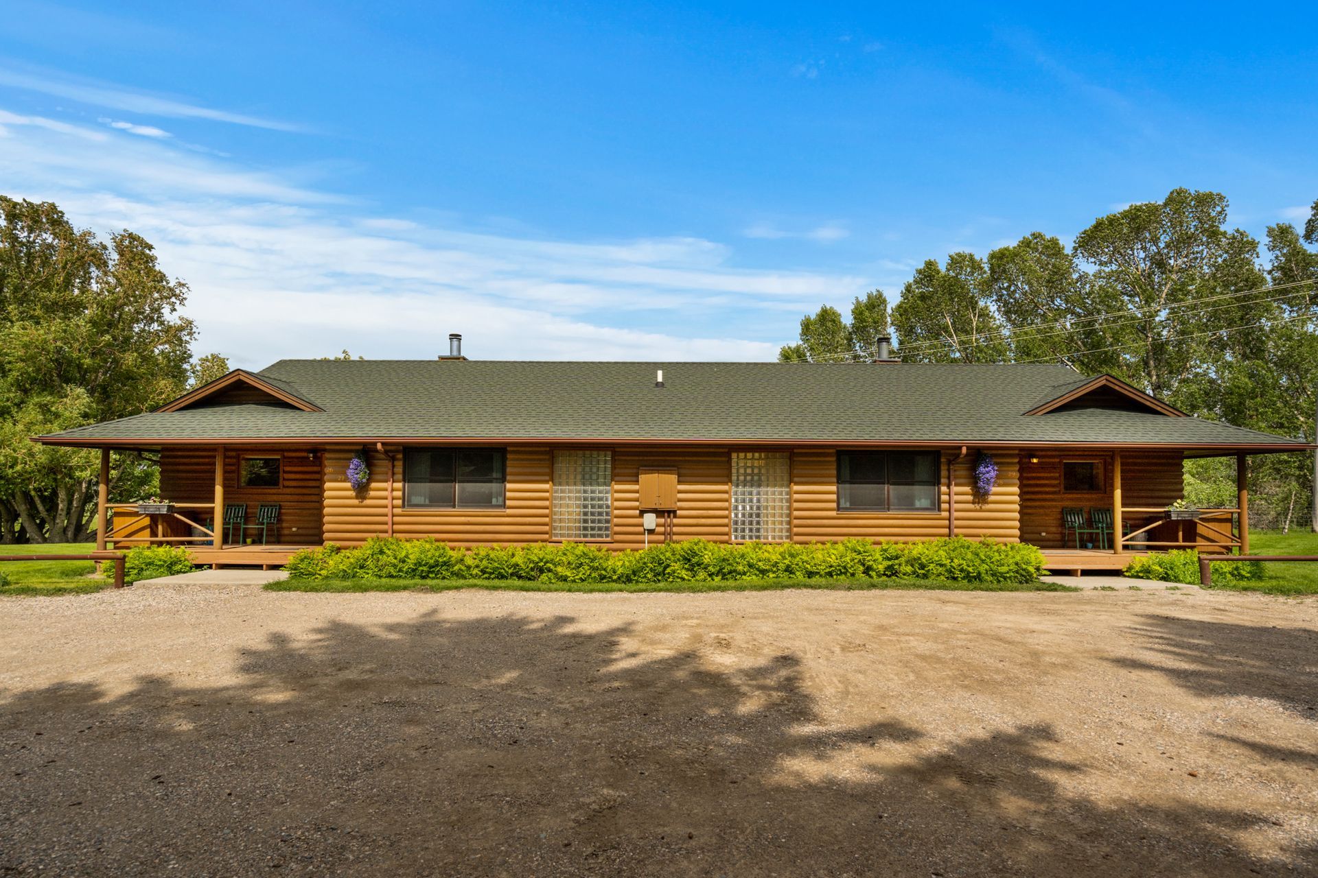 A large log cabin with a green roof is sitting on top of a dirt field.