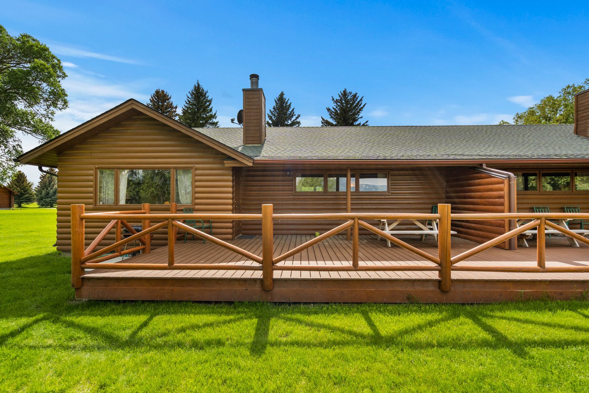 A log cabin with a wooden deck and fence in front of it.