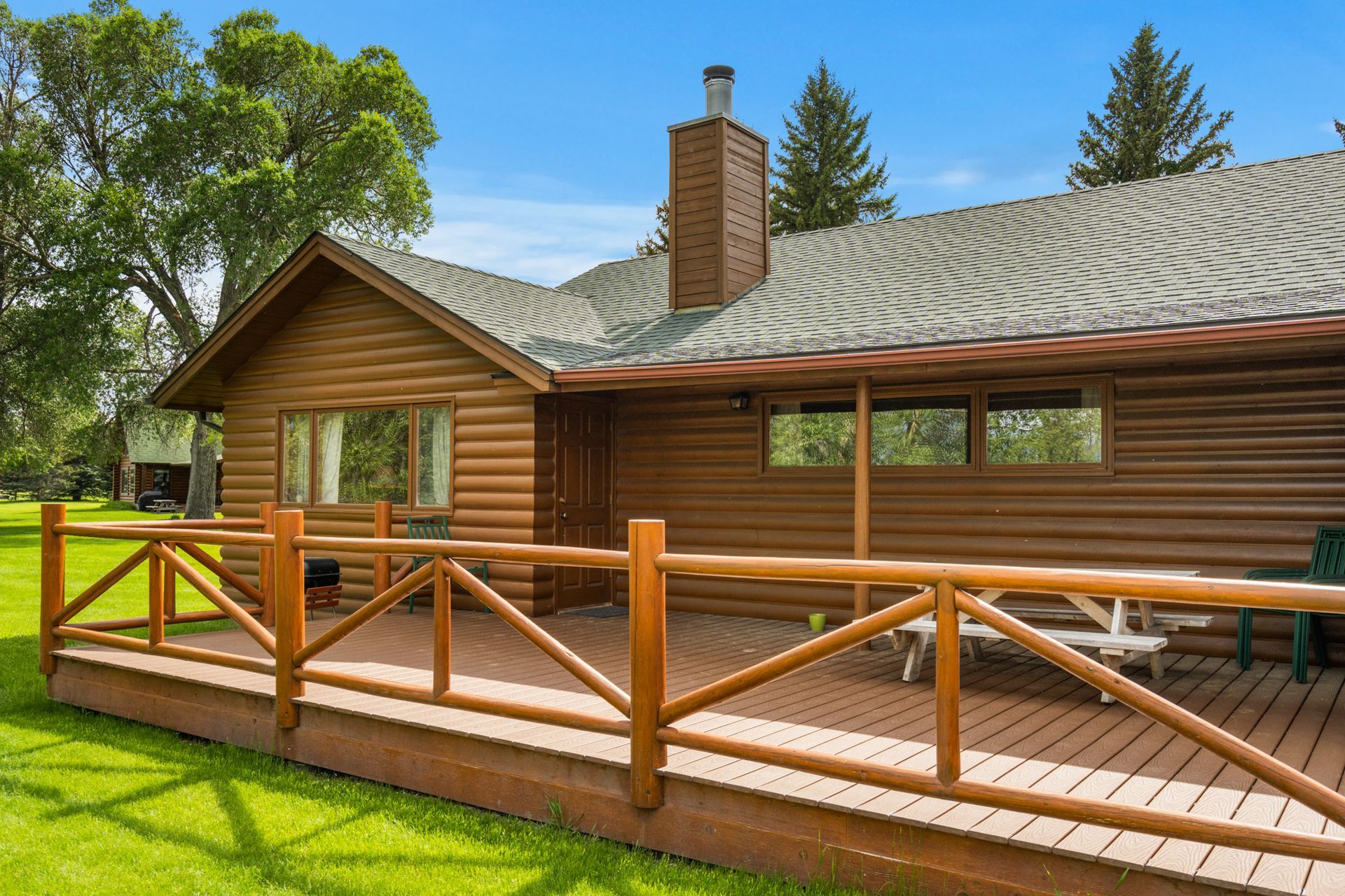 A log cabin with a wooden deck and fence in front of it.