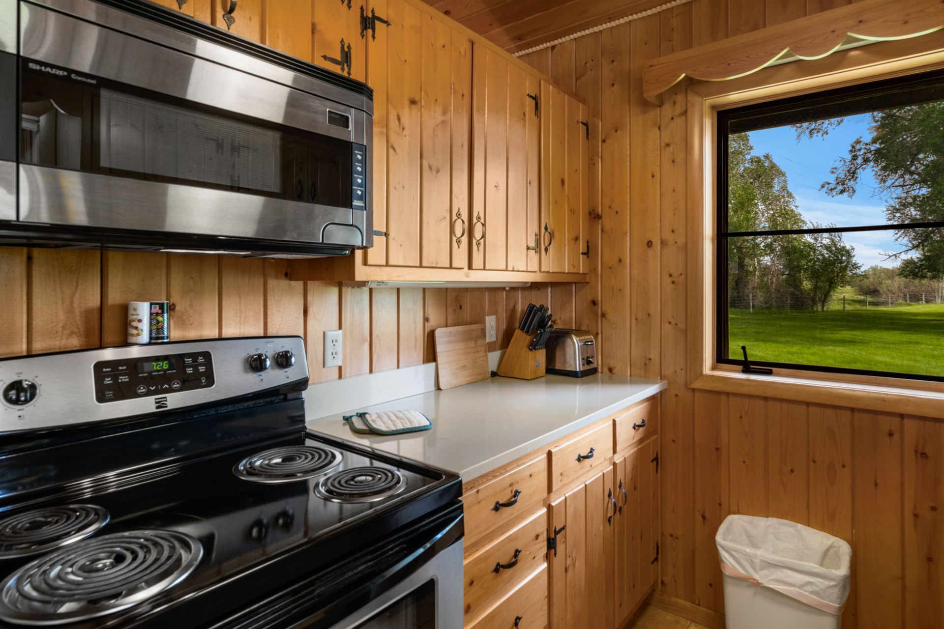 A kitchen with a stove , microwave , and trash can