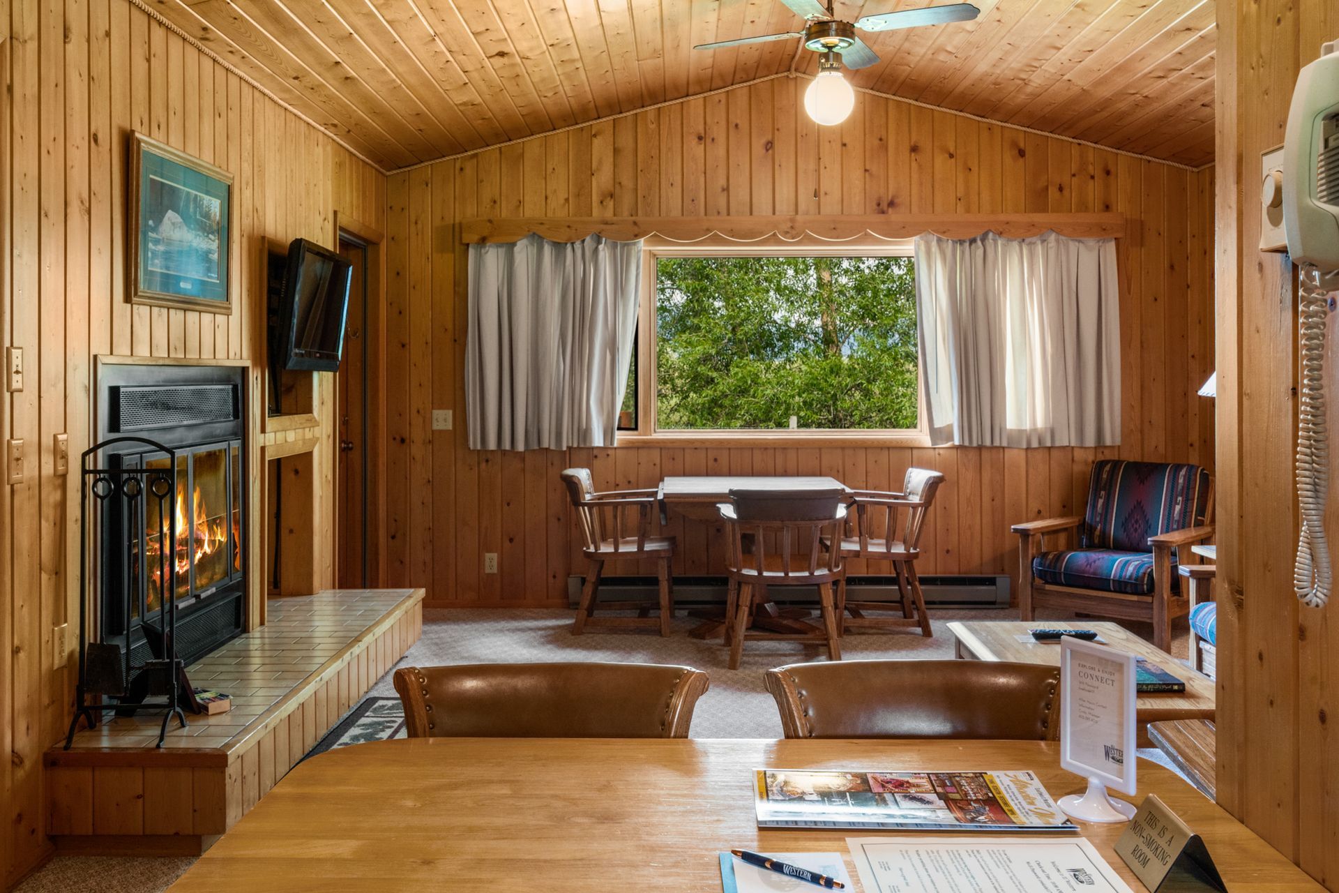 A living room with a fireplace , table , chairs and a ceiling fan.