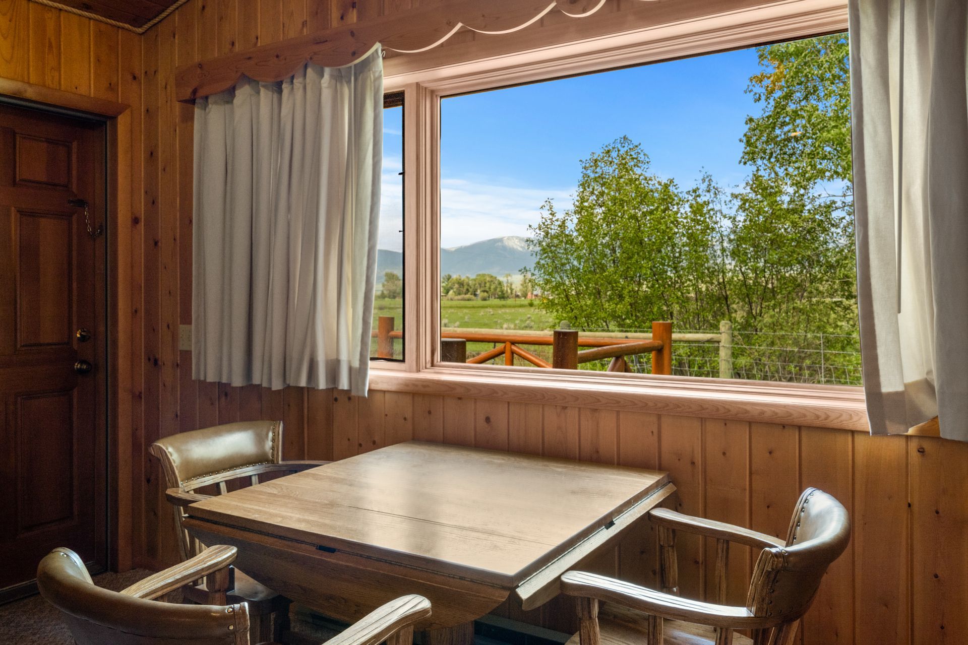 There is a table and chairs in front of a window with a view of a field.