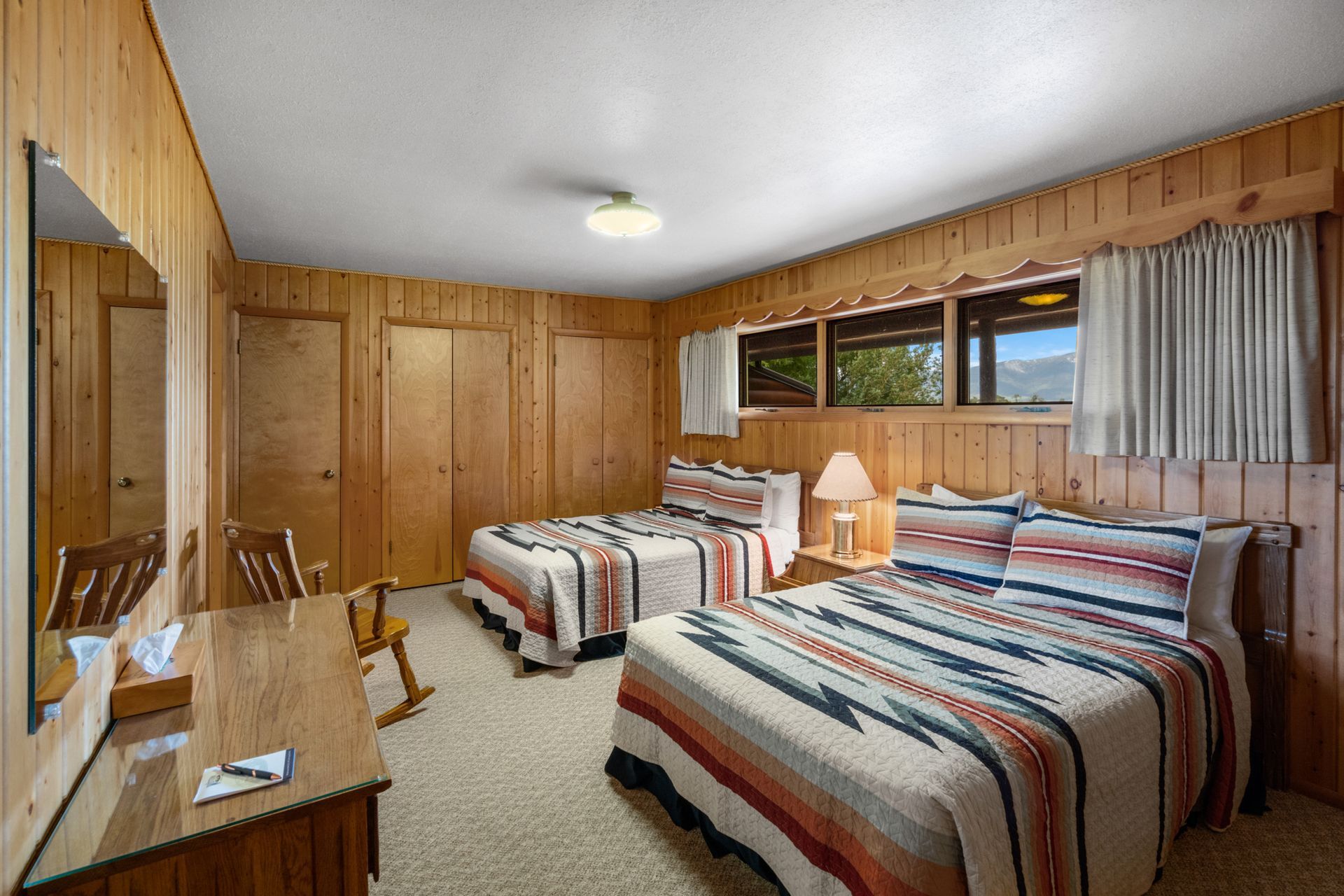 A hotel room with two beds , a desk , and a rocking chair.