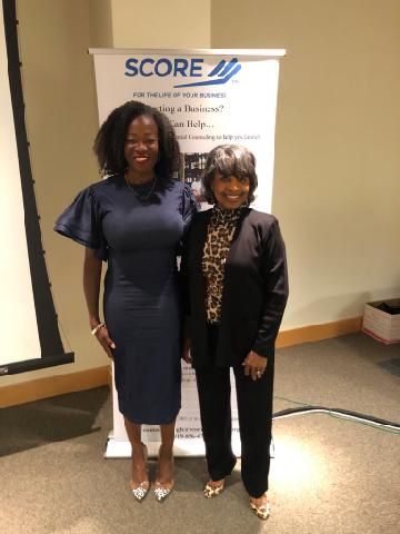 MiMi K and Patti Williams are standing next to each other in front of a score sign.