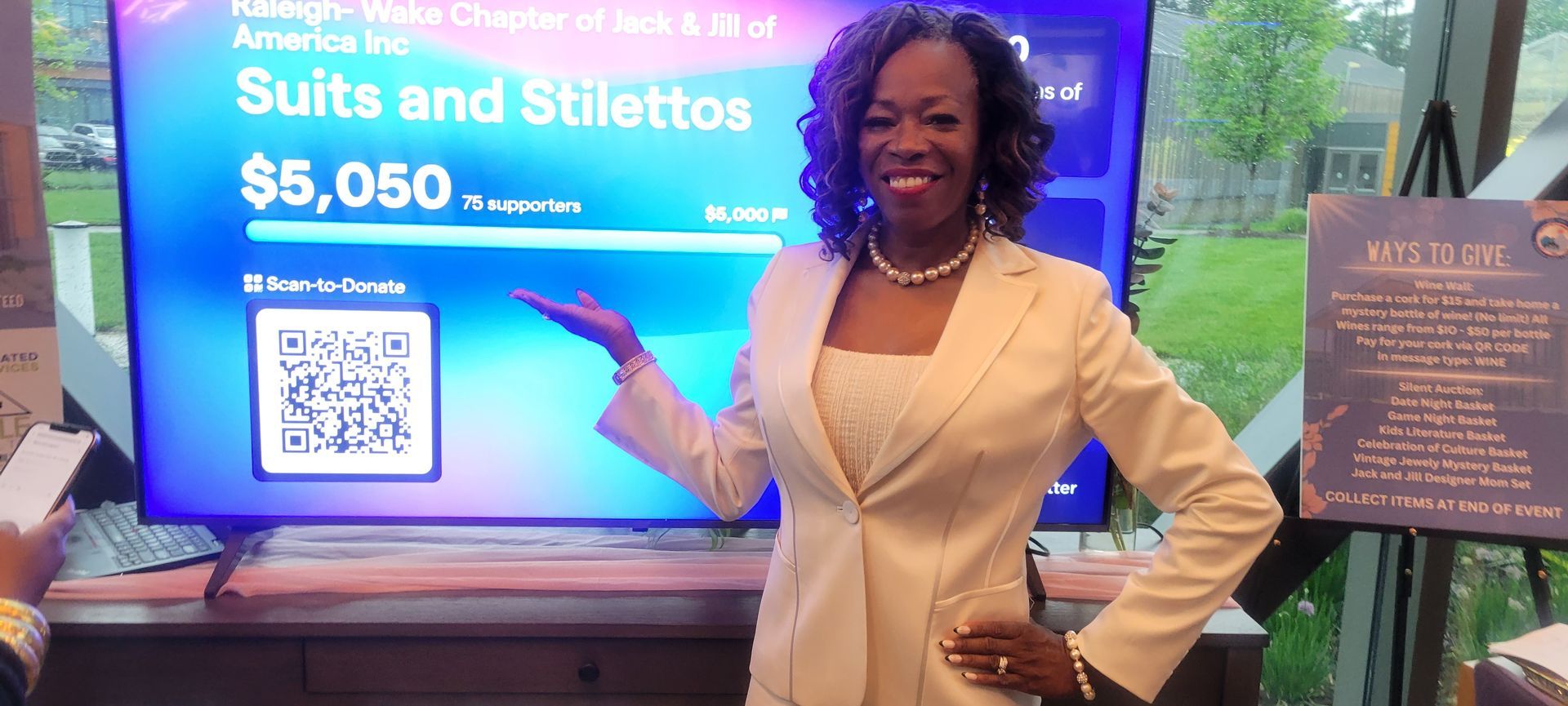 MiMi K in a suit is standing in front of a television.