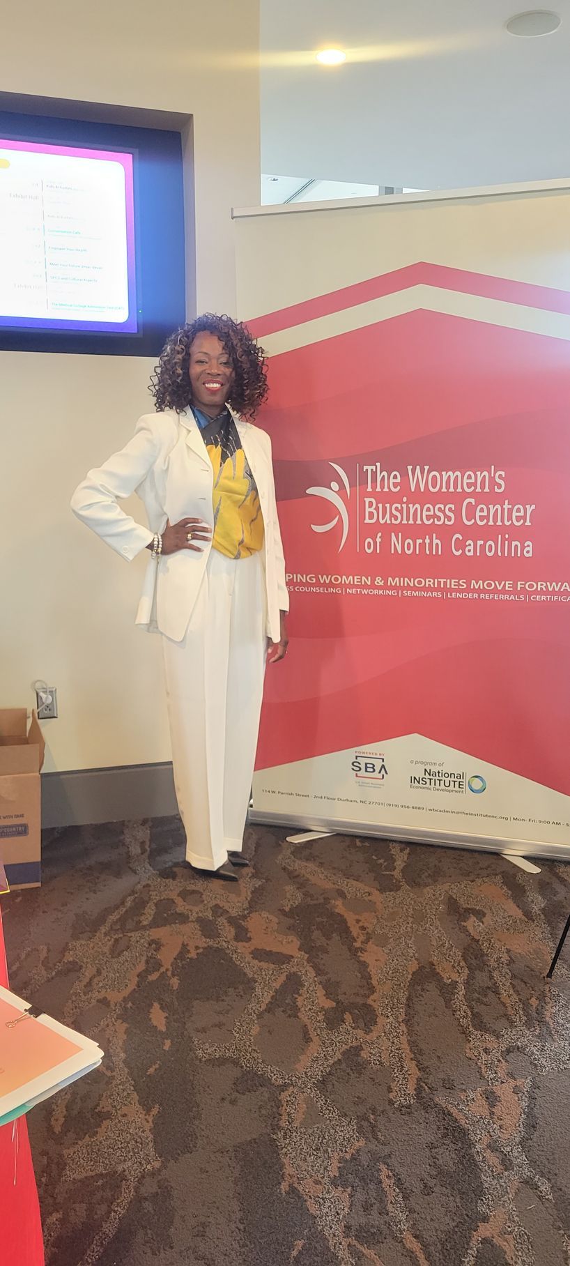 MiMi K in a white suit is standing in front of a red sign.