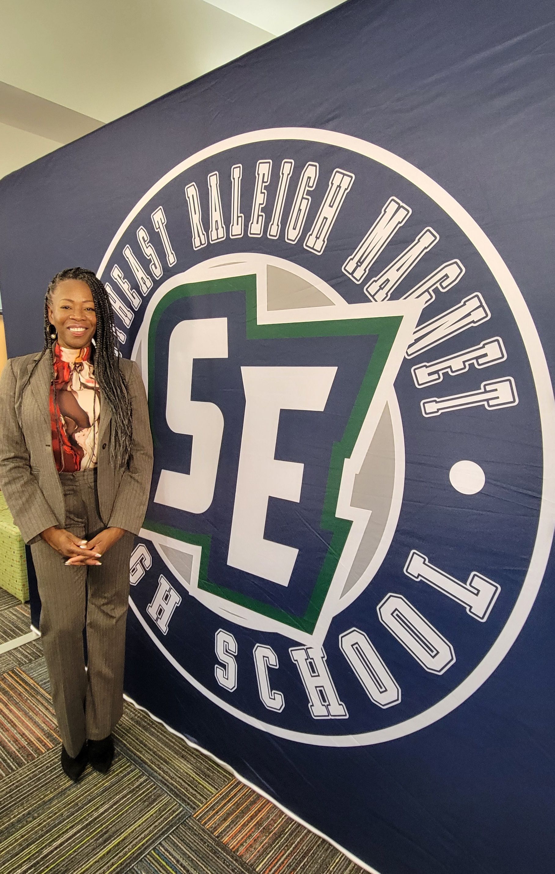 MiMi K in a suit is standing in front of a school logo.