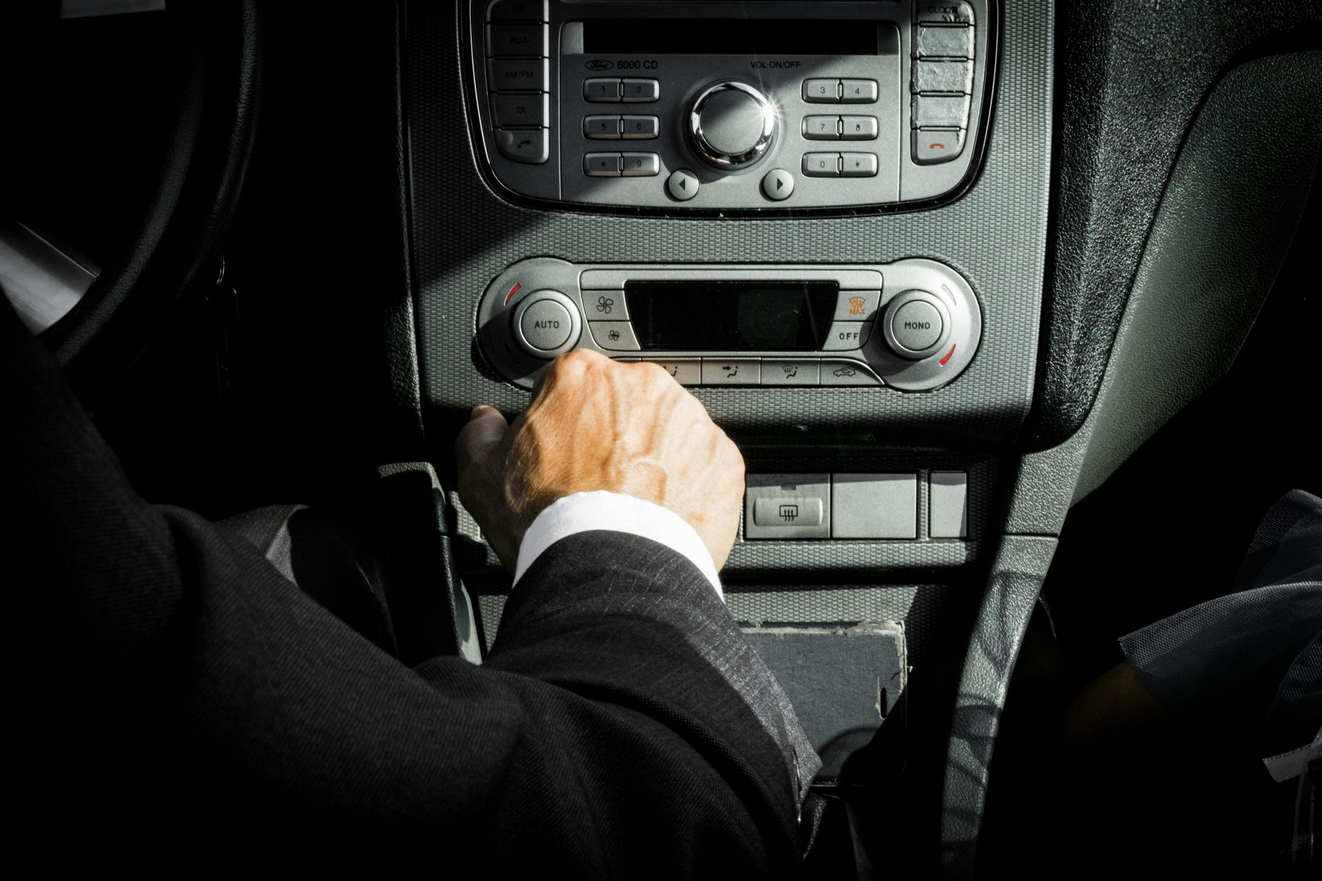 A man in a suit is adjusting the radio in his car