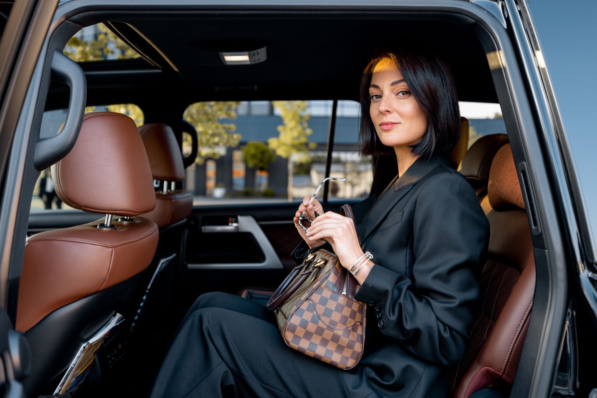 A woman is sitting in the back seat of a car holding a purse.