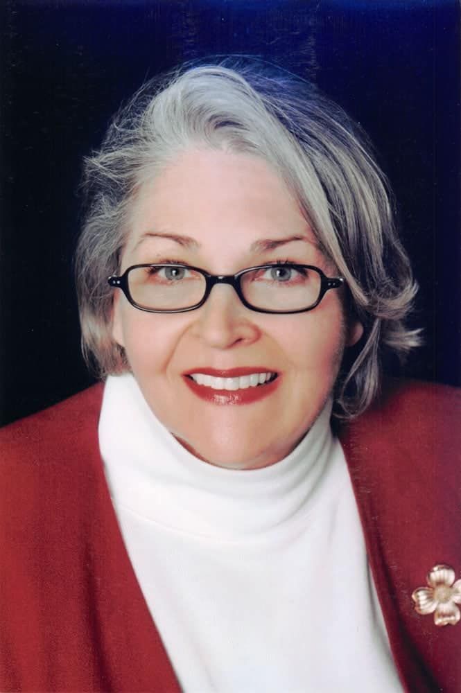 A photo of a woman wearing glasses and a white turtleneck smiles for the camera.