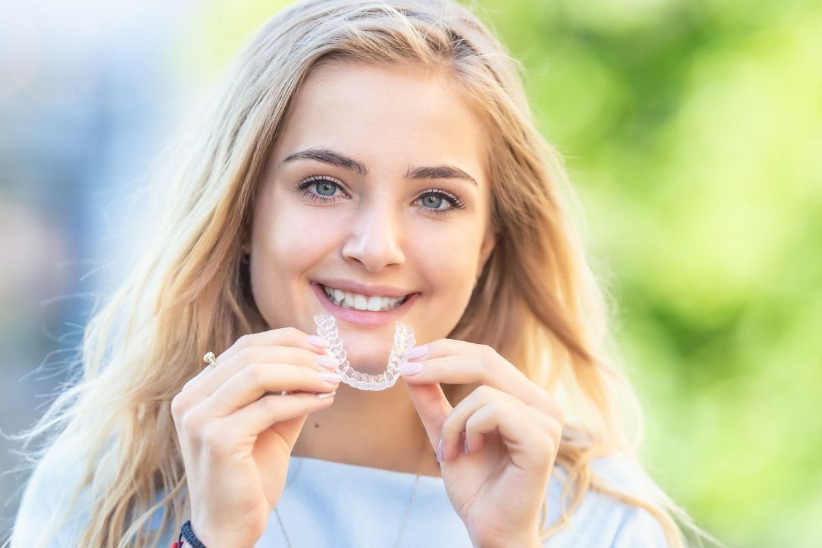 A young woman is holding a clear retainer in her hands and smiling.