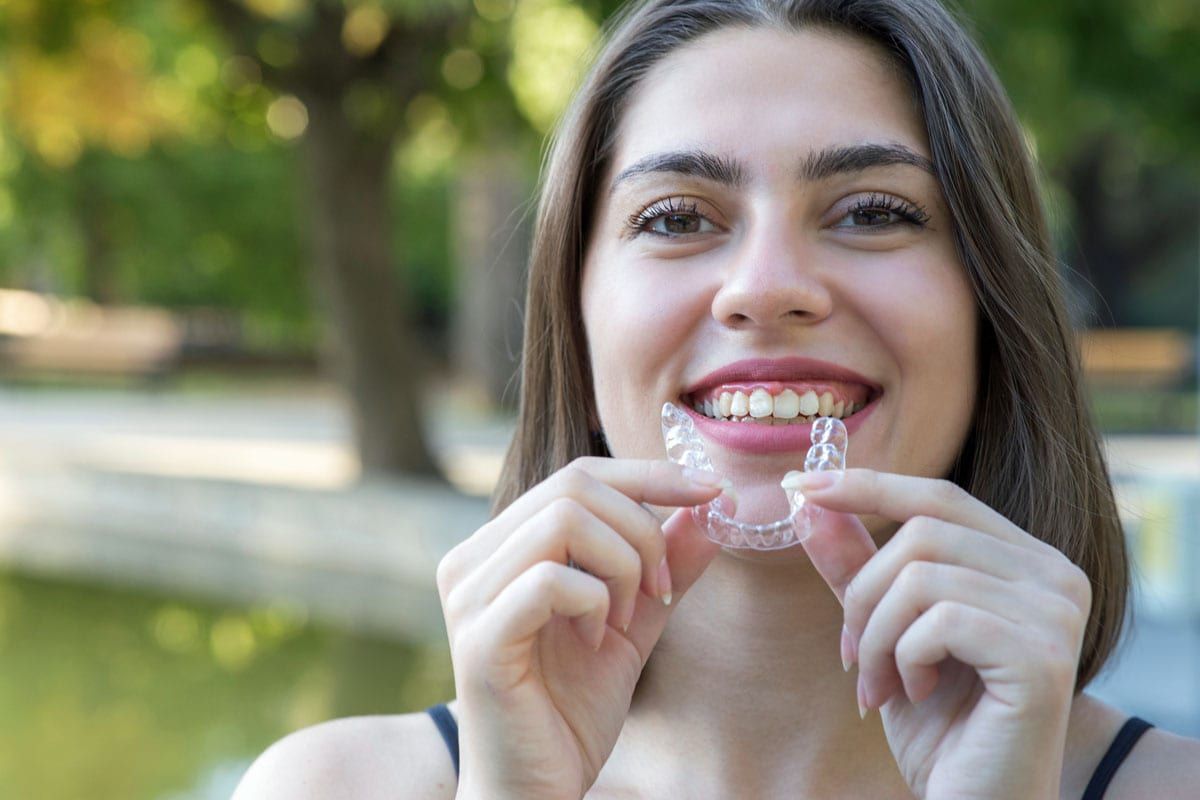 A woman is holding a clear Invisalign in her hands and smiling .