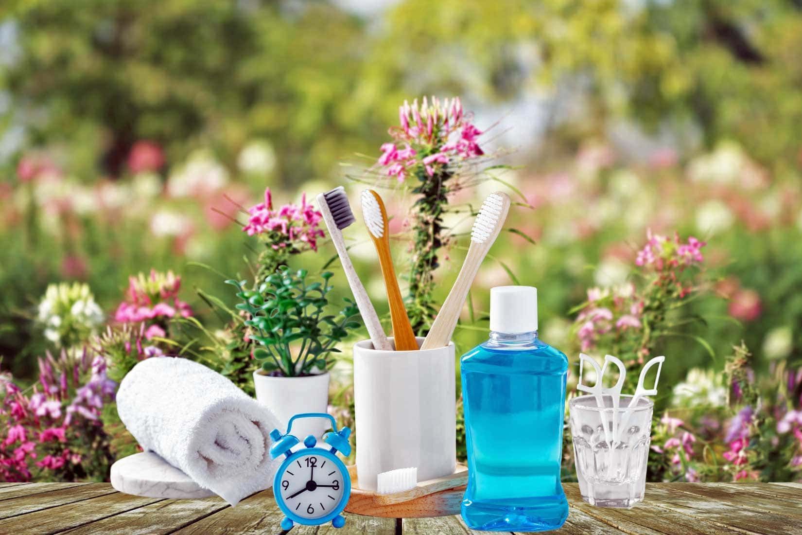A wooden table topped with toothbrushes , mouthwash , towels and a clock.