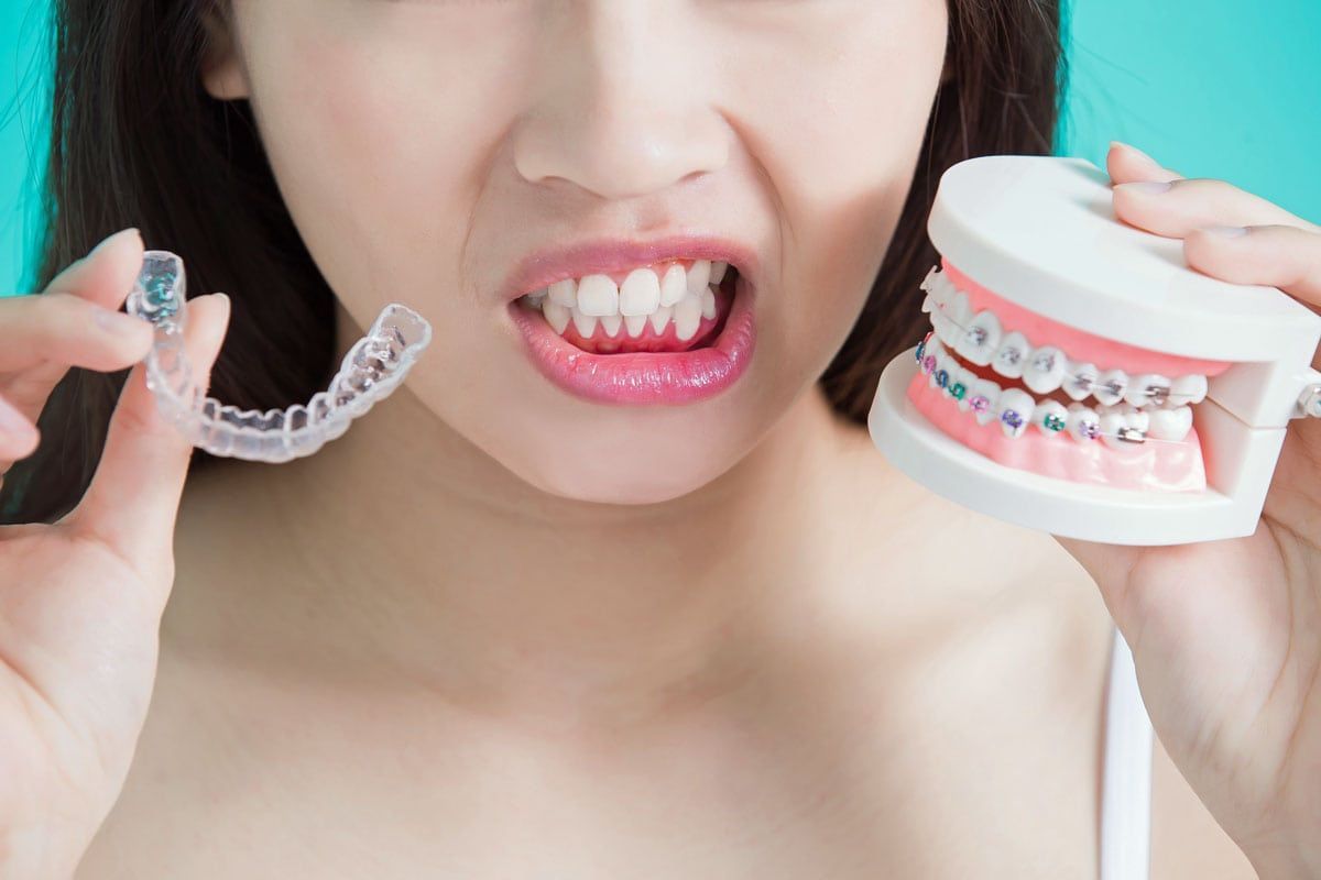 a woman is holding a clear retainer and a model of her teeth with braces .