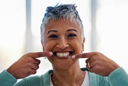 Photo of a woman smiling and pointing at her teeth.