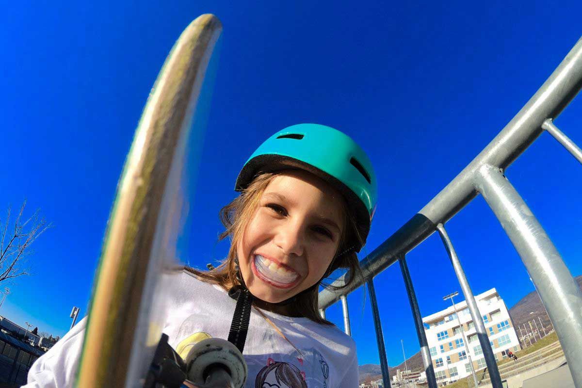 A young girl wearing a helmet and holding a skateboard.