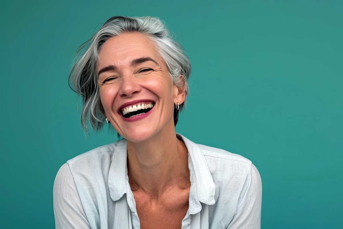 a woman with gray hair is smiling with her eyes closed against a blue background .