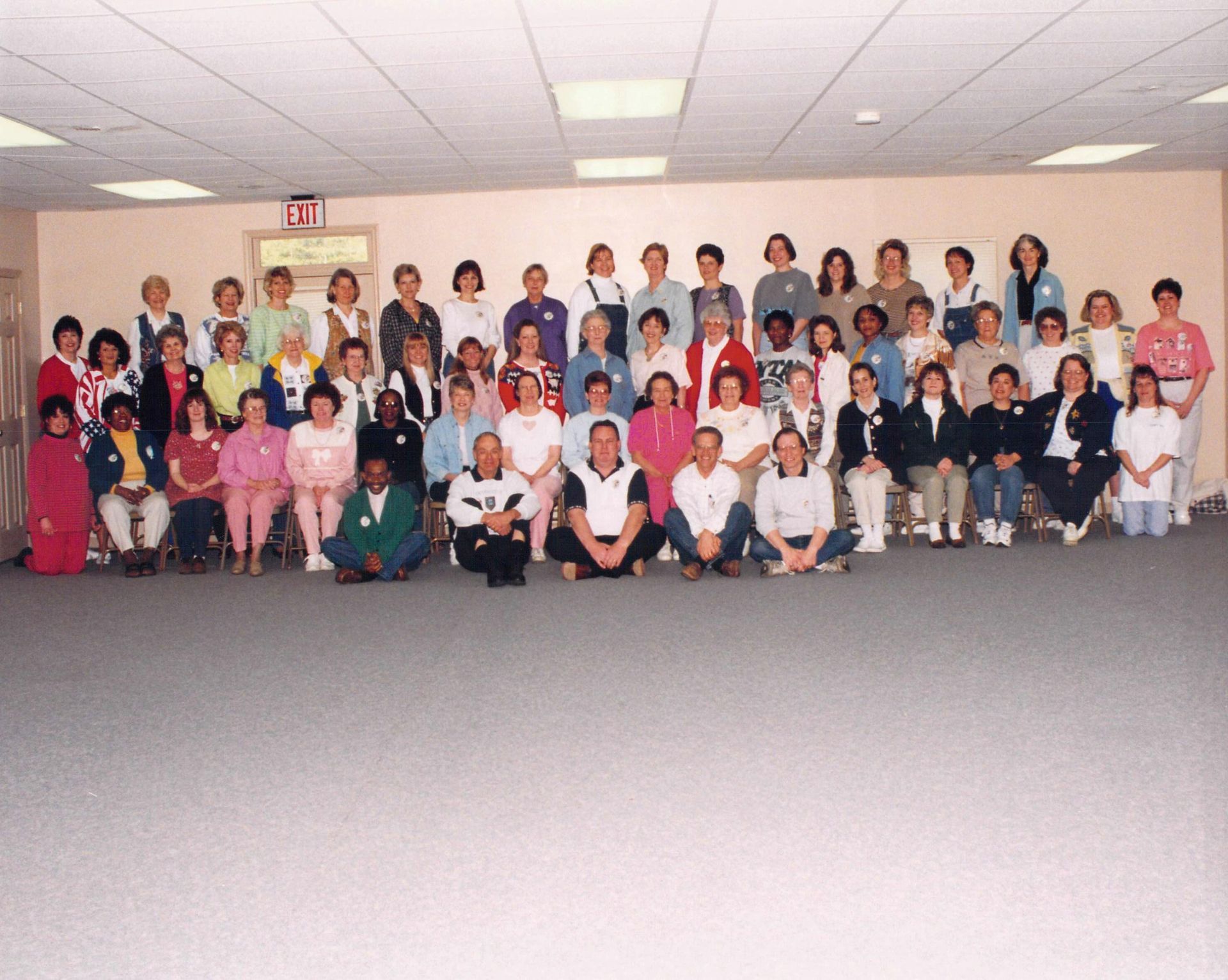A large group of people pose for a photo in a room with an exit sign