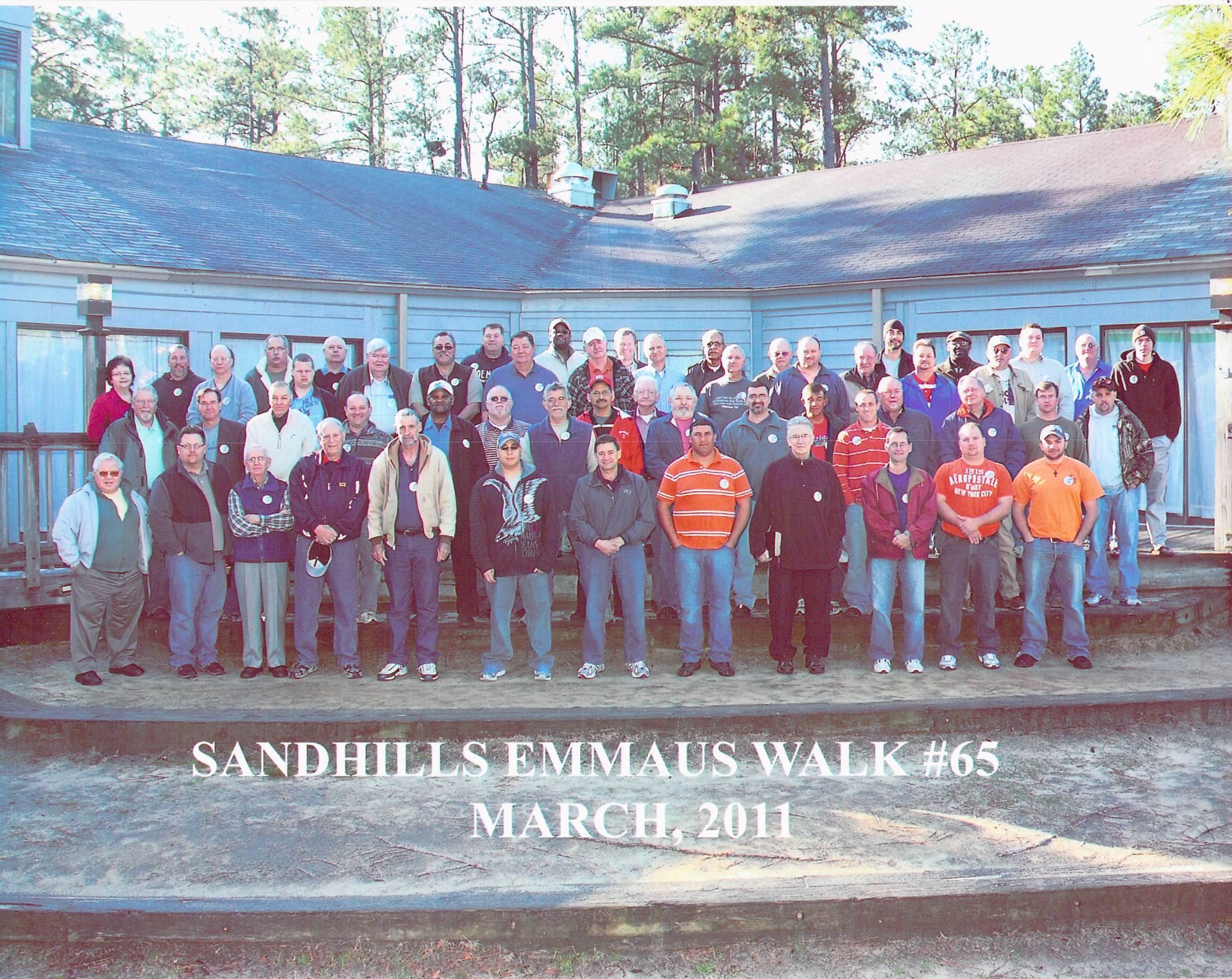 A group of people standing in front of a building that says sandhills emmaus walk 65 march 2011