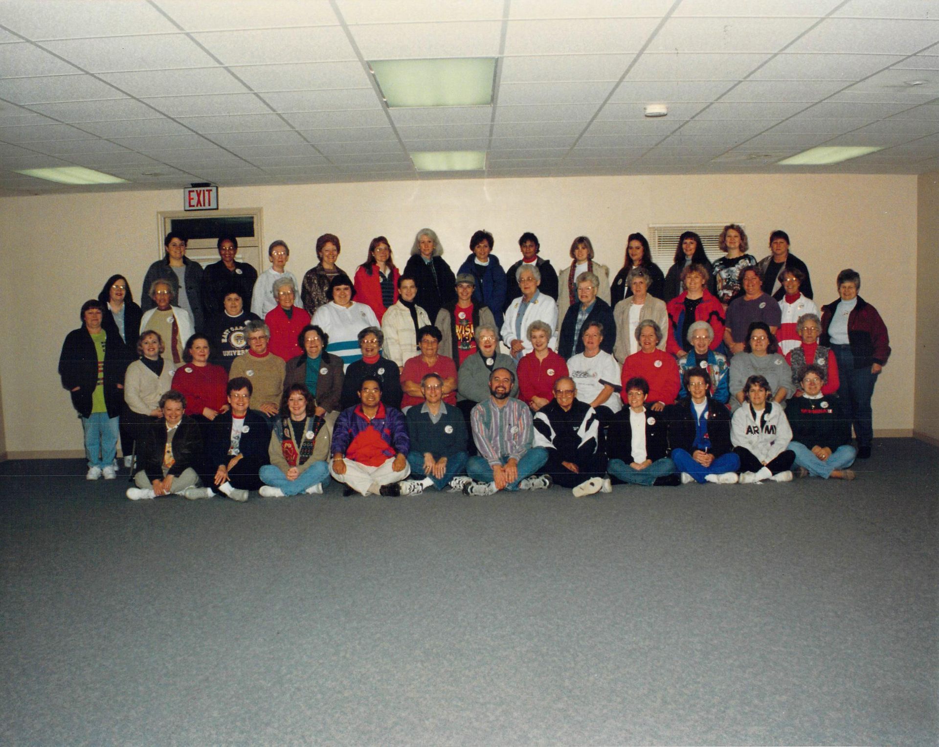 A large group of people are posing for a picture in a room with an exit sign on the wall
