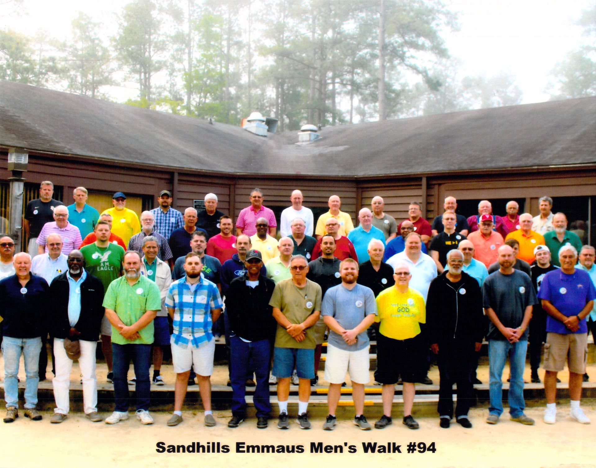 A group of men standing in front of a building that says sandhills emmaus men 's walk # 94