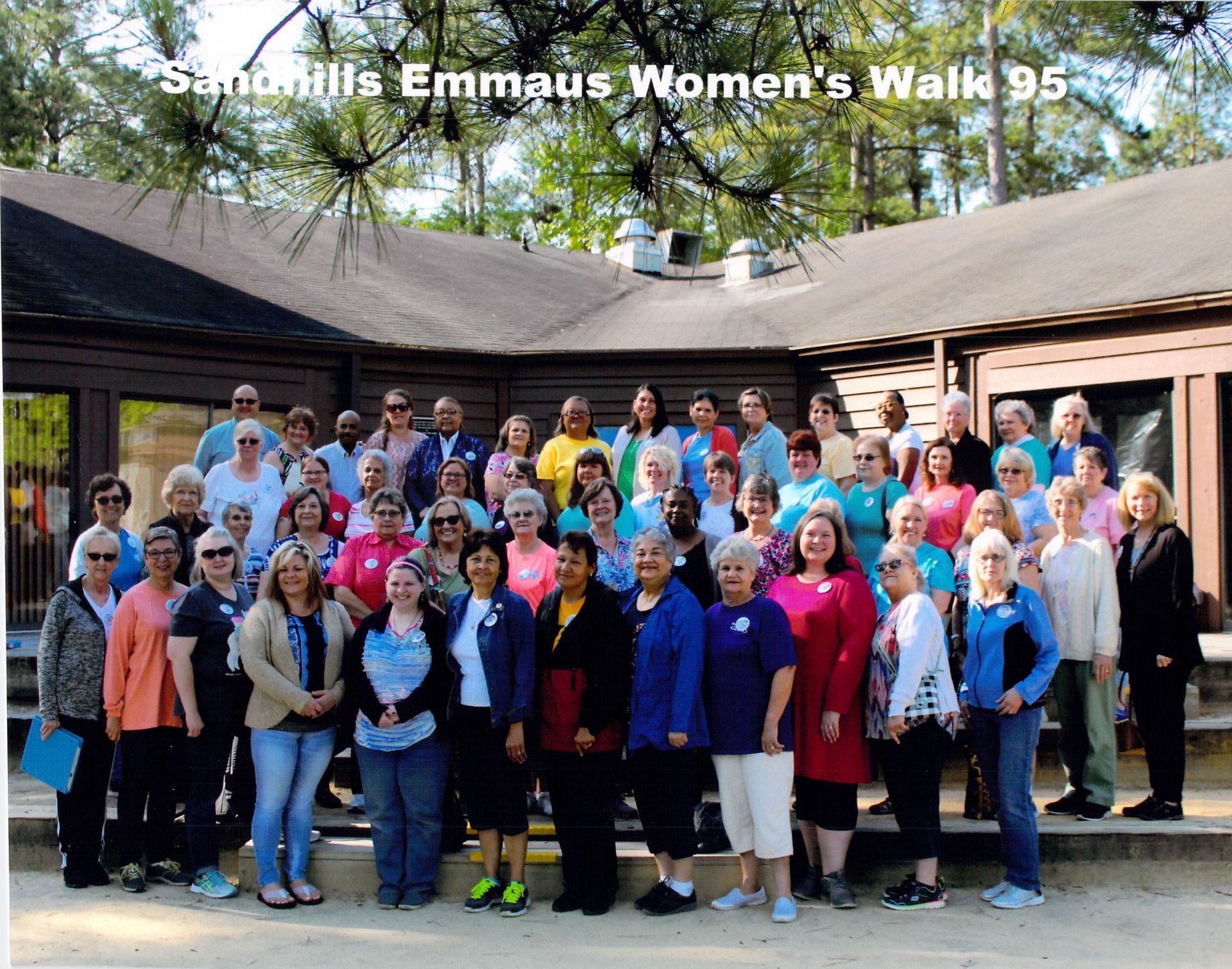 A group of women standing in front of a building that says emmaus women 's walk 95
