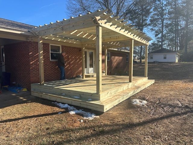 Newly built wooden deck with pergola attached to a brick house; person working near window.